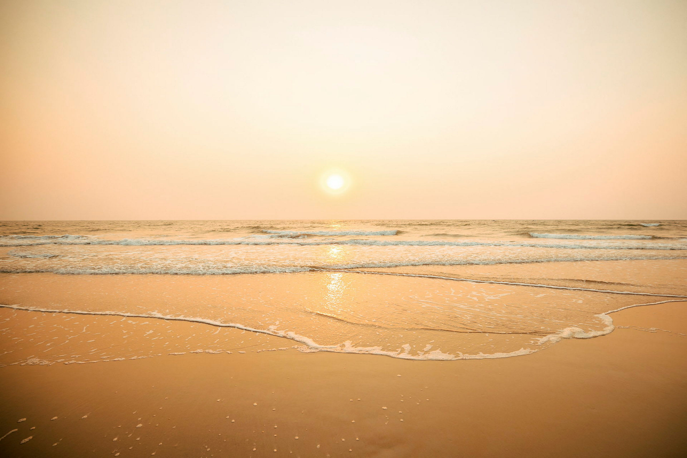 En solnedgang over havet med bølger, der når en sandstrand. (AI-genereret tekst)