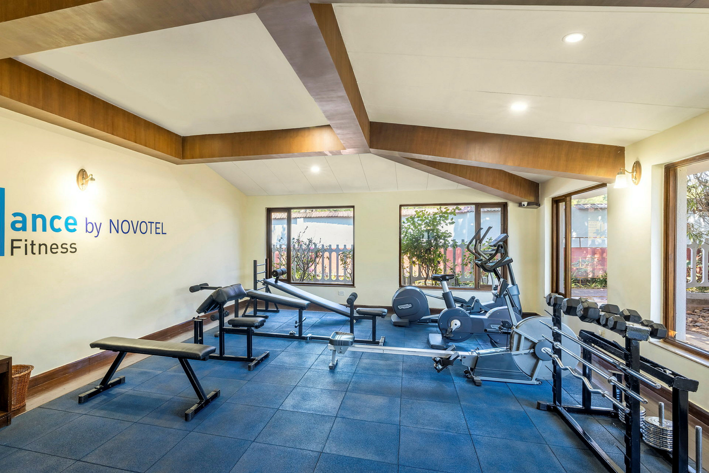 Et fitnesscenter med træningsudstyr, vinduer og et skilt med teksten 'Balance by NOVOTEL Fitness'. (AI-genereret tekst)