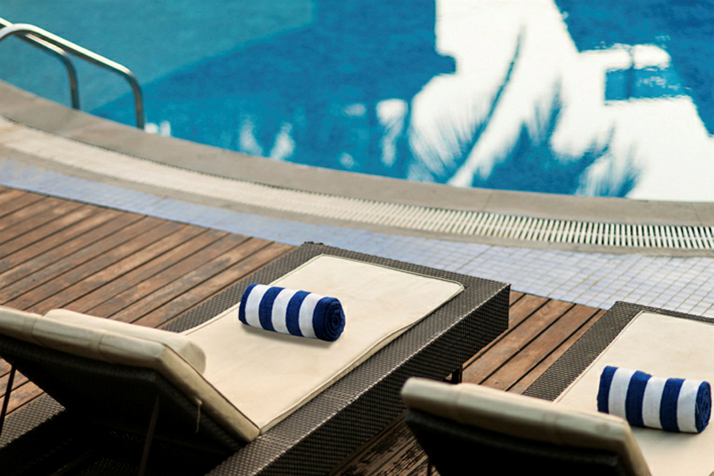 To liggestole med stribede håndklæder står på en træterrasse ved siden af en pool. (AI-genereret tekst)