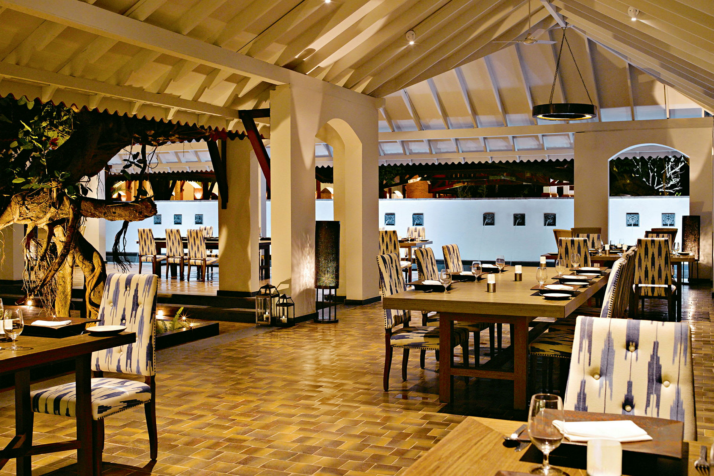 Interiøret af en restaurant med siddepladser ved opdækkede borde og et træ i midten. (AI-genereret tekst)