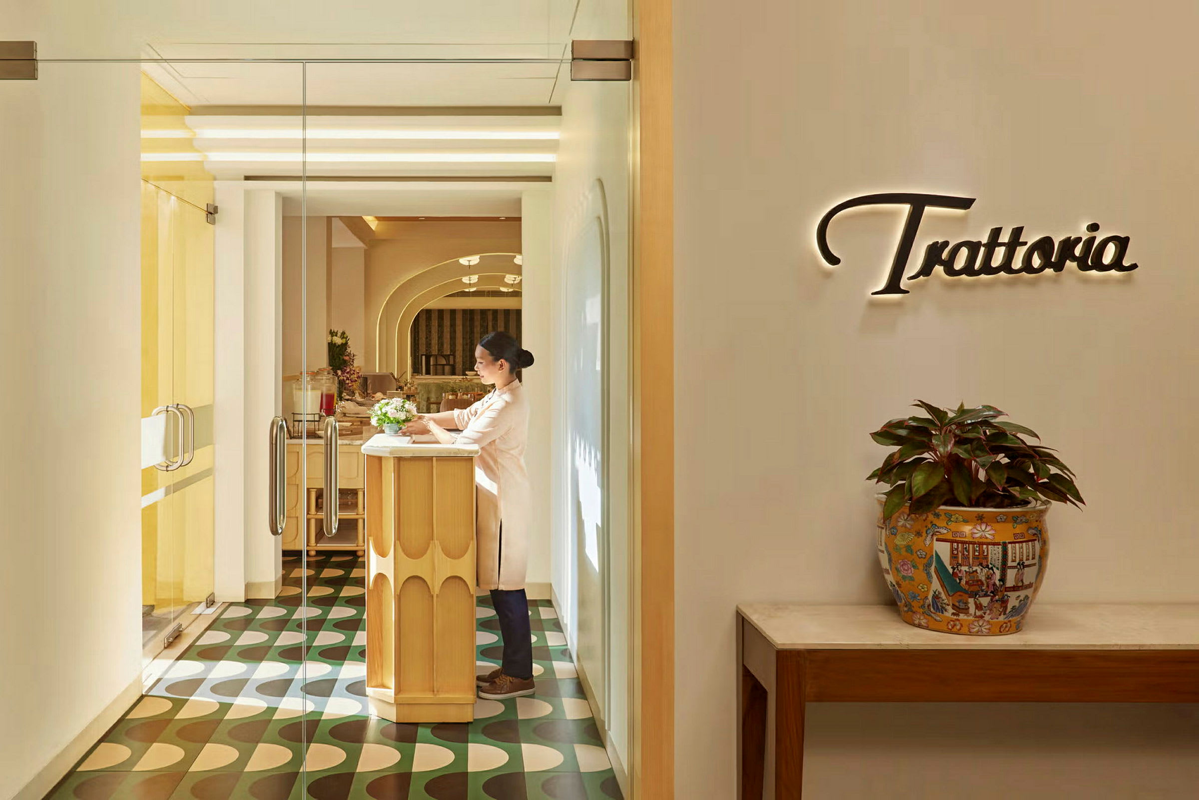 Indgangen til en restaurant med ordet 'Trattoria' på væggen og et bord med potteplante. (AI-genereret tekst)