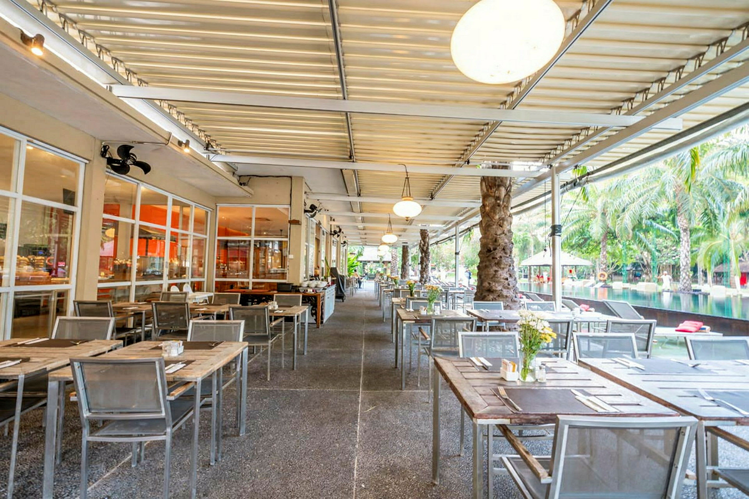 En udendørsrestaurant med borde og stole opstillet under et overdækket tag. (AI-genereret tekst)