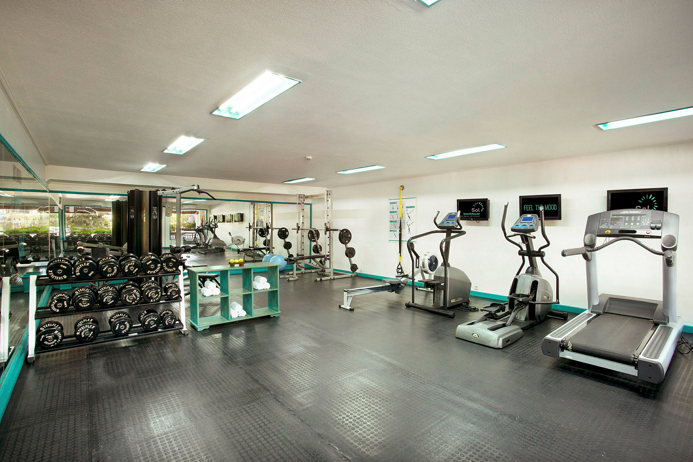 Fitnesscenter med træningsmaskiner, frie vægte og spejlvæg. (AI-genereret tekst)