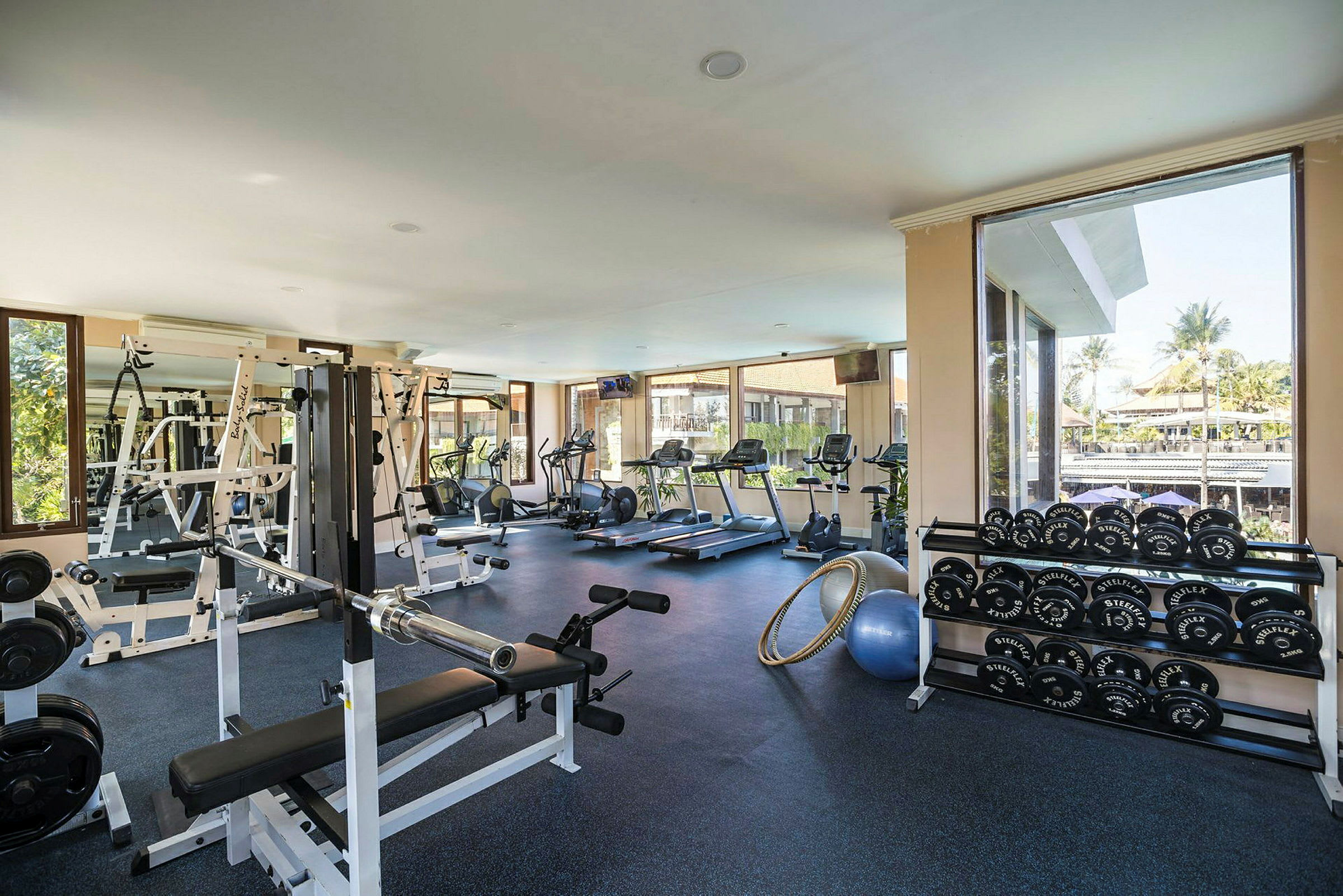 Fitnesscenter med træningsudstyr og vinduer, der viser udsigt udendørs. (AI-genereret tekst)