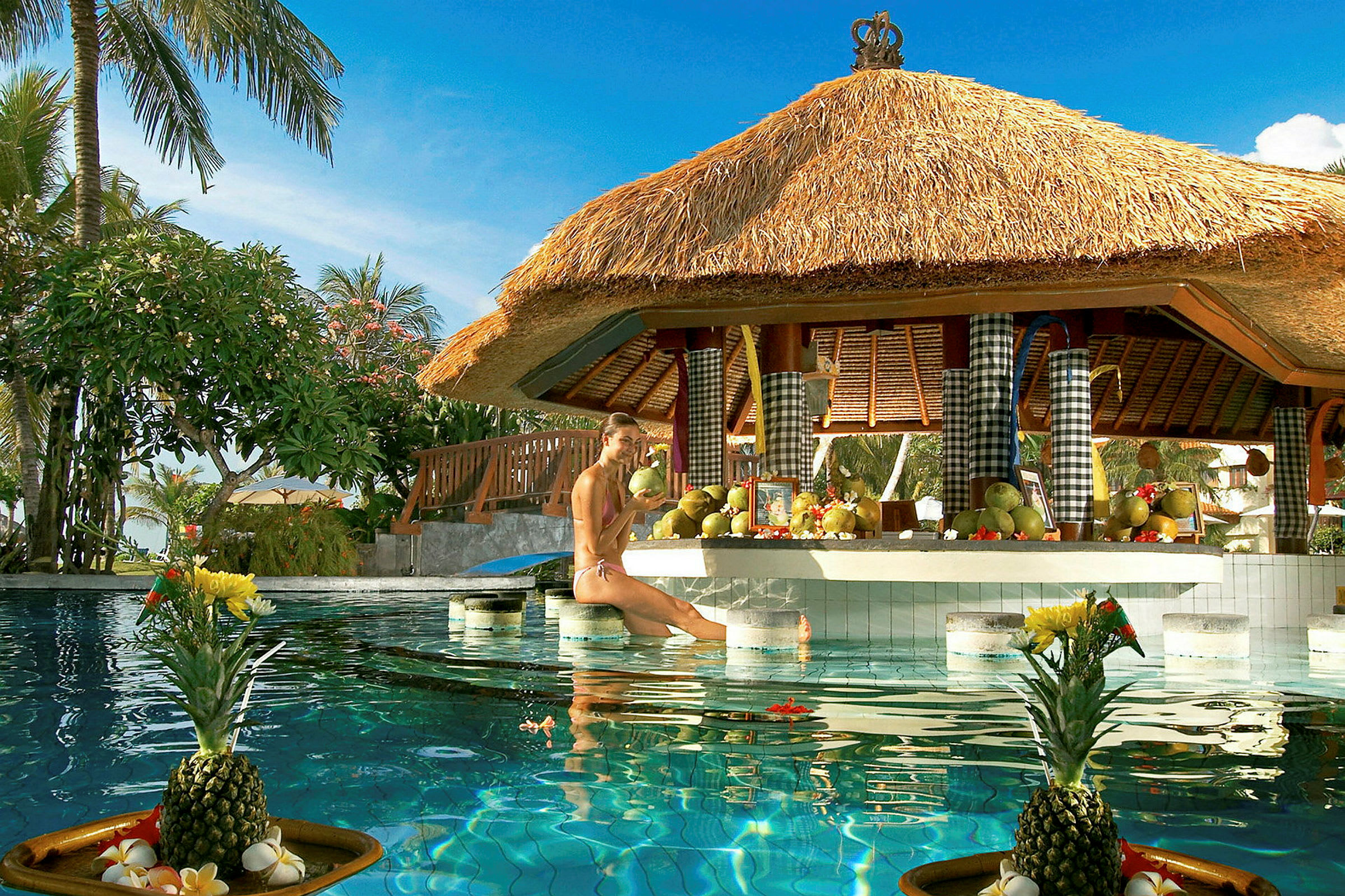 Billede af en poolbar med stråtag og et bord dekoreret med frugter, samt en opstillet ananas i forgrunden. (AI-genereret tekst)