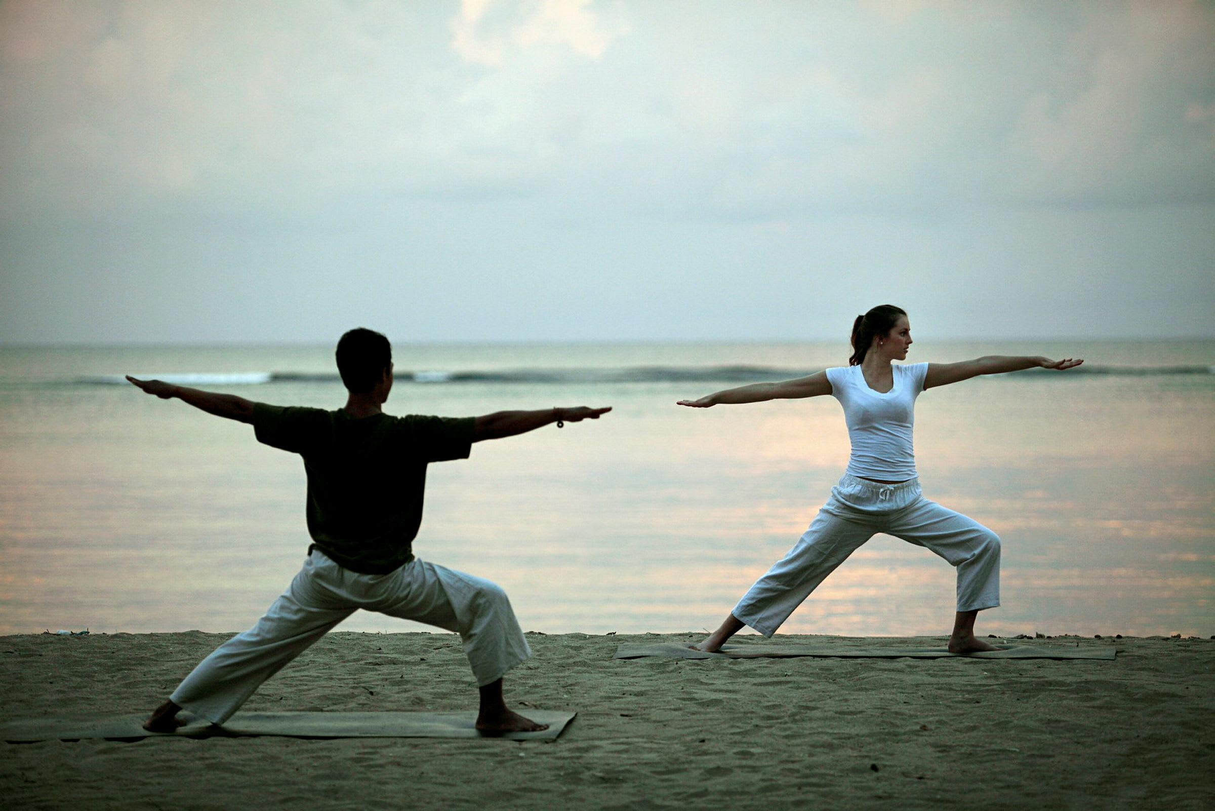 To personer udfører yogapositioner på stranden med havet i baggrunden. (AI-genereret tekst)