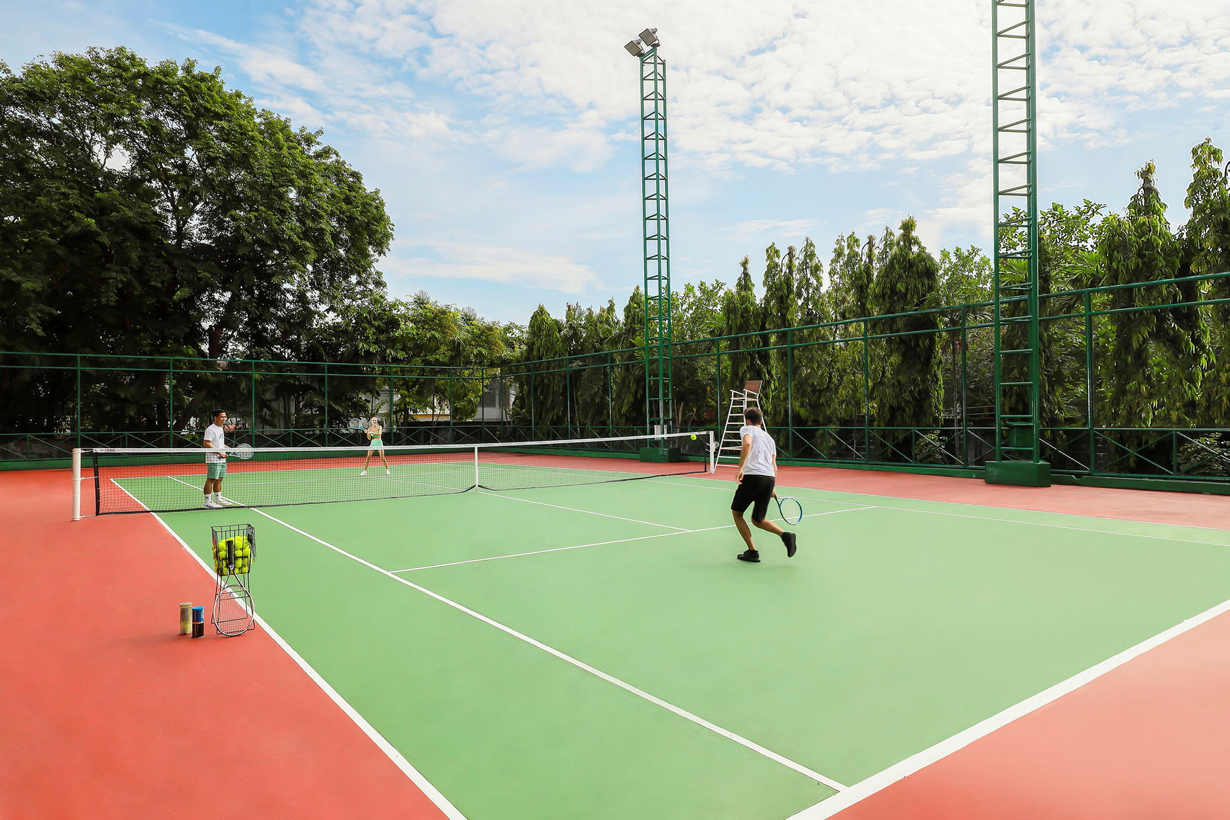 Personer spiller tennis på en udendørs bane. Træer ses i baggrunden. (AI-genereret tekst)