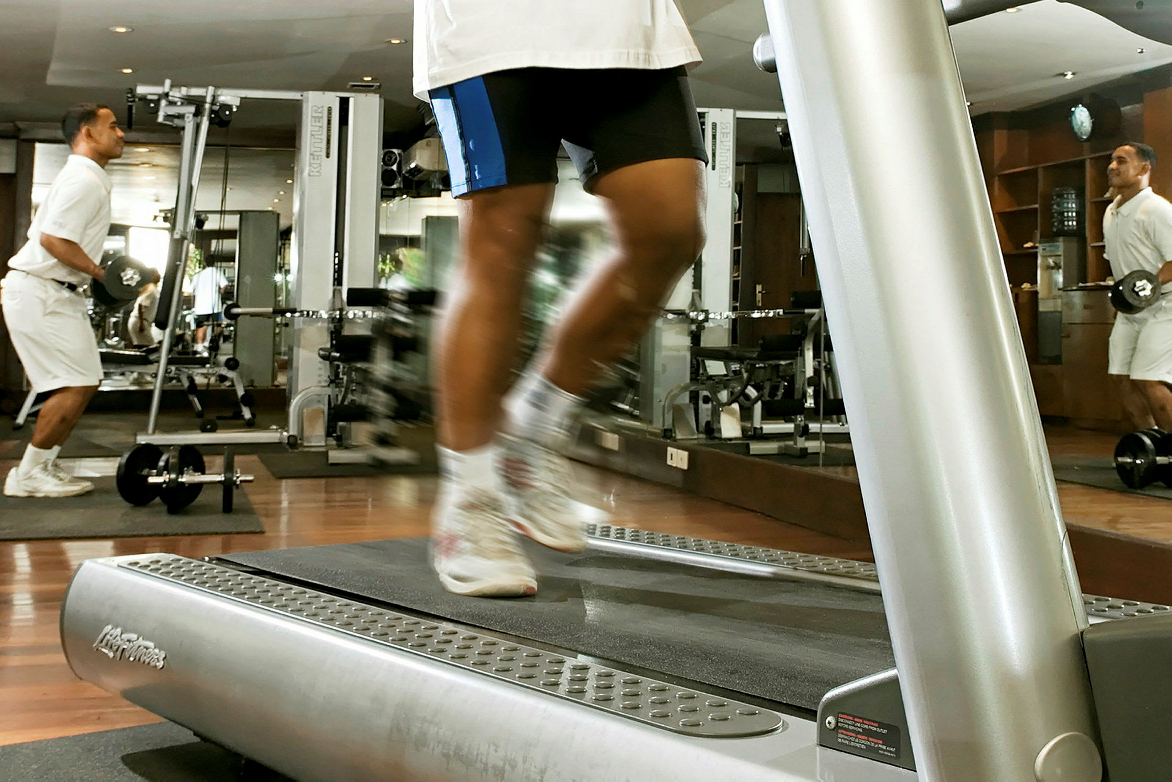 Et fitnesscenter med træningsmaskiner, hvor en person løber på et løbebånd. (AI-genereret tekst)