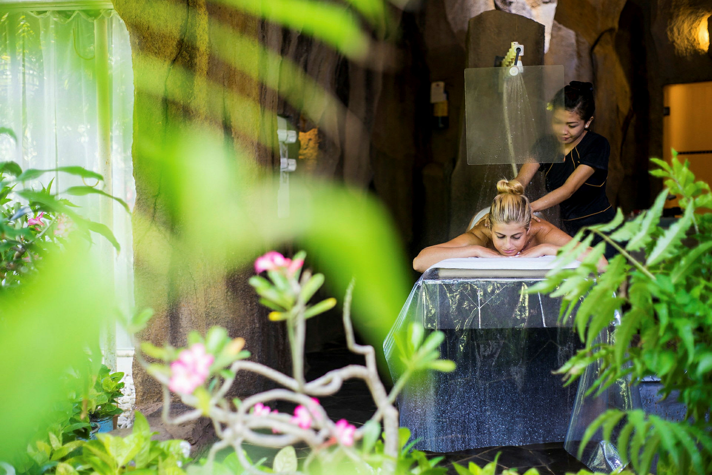 En person får massage i en naturlig atmosfære omgivet af grønne planter. (AI-genereret tekst)