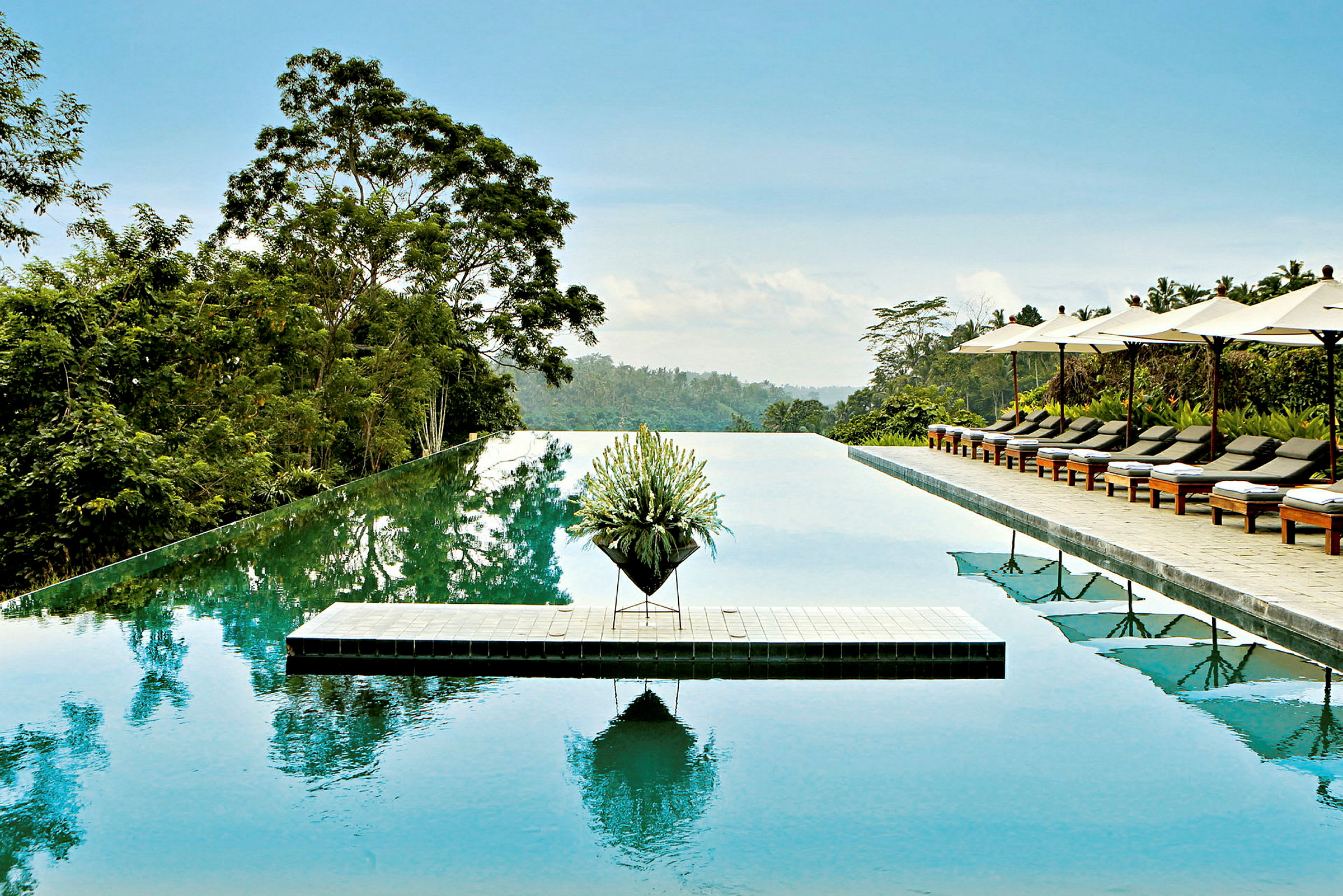 Infinity-pool med frodige omgivelser, liggestole og parasoller til højre. (AI-genereret tekst)