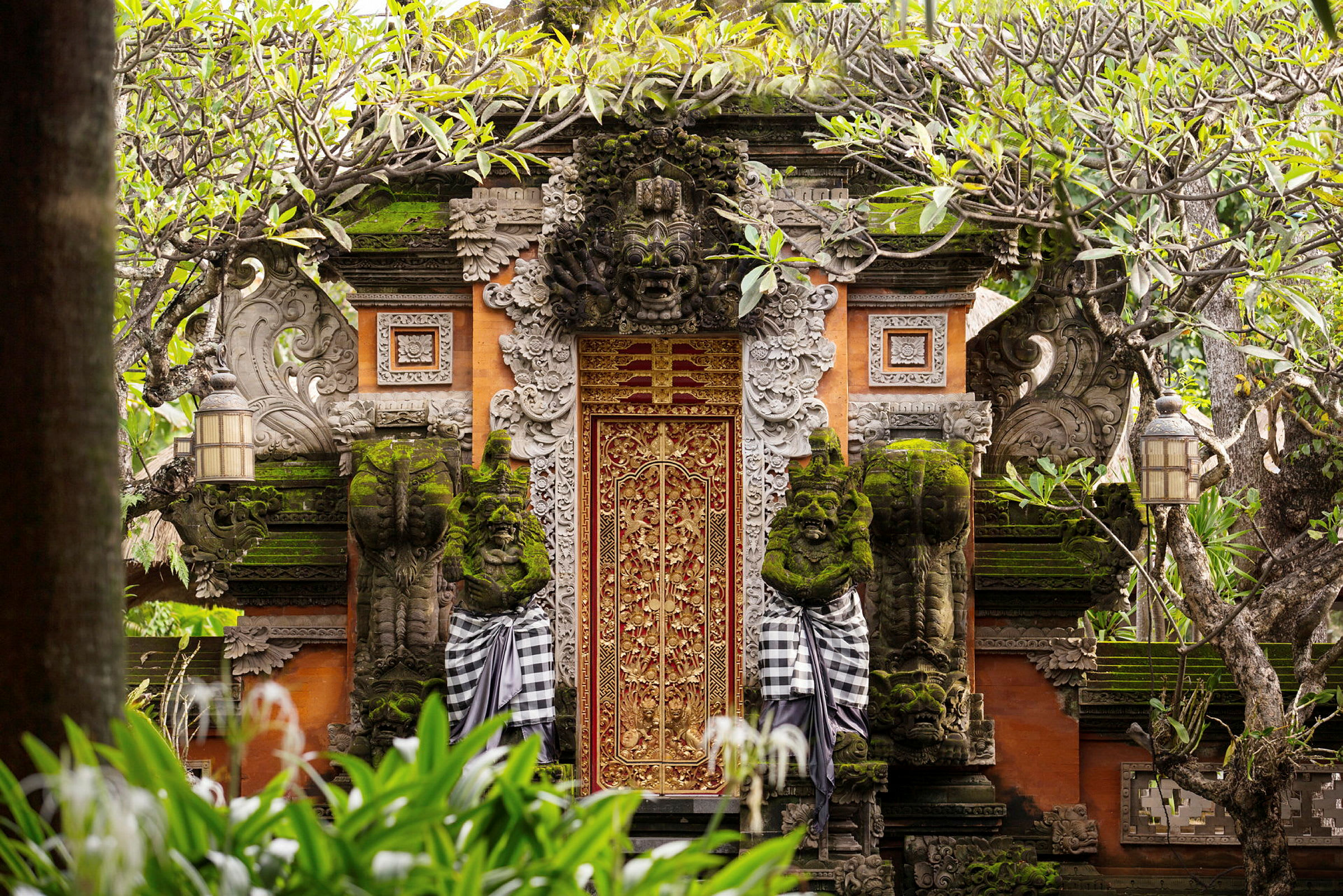 Dekorativt udsmykket port omgivet af grønne planter og træer. (AI-genereret tekst)