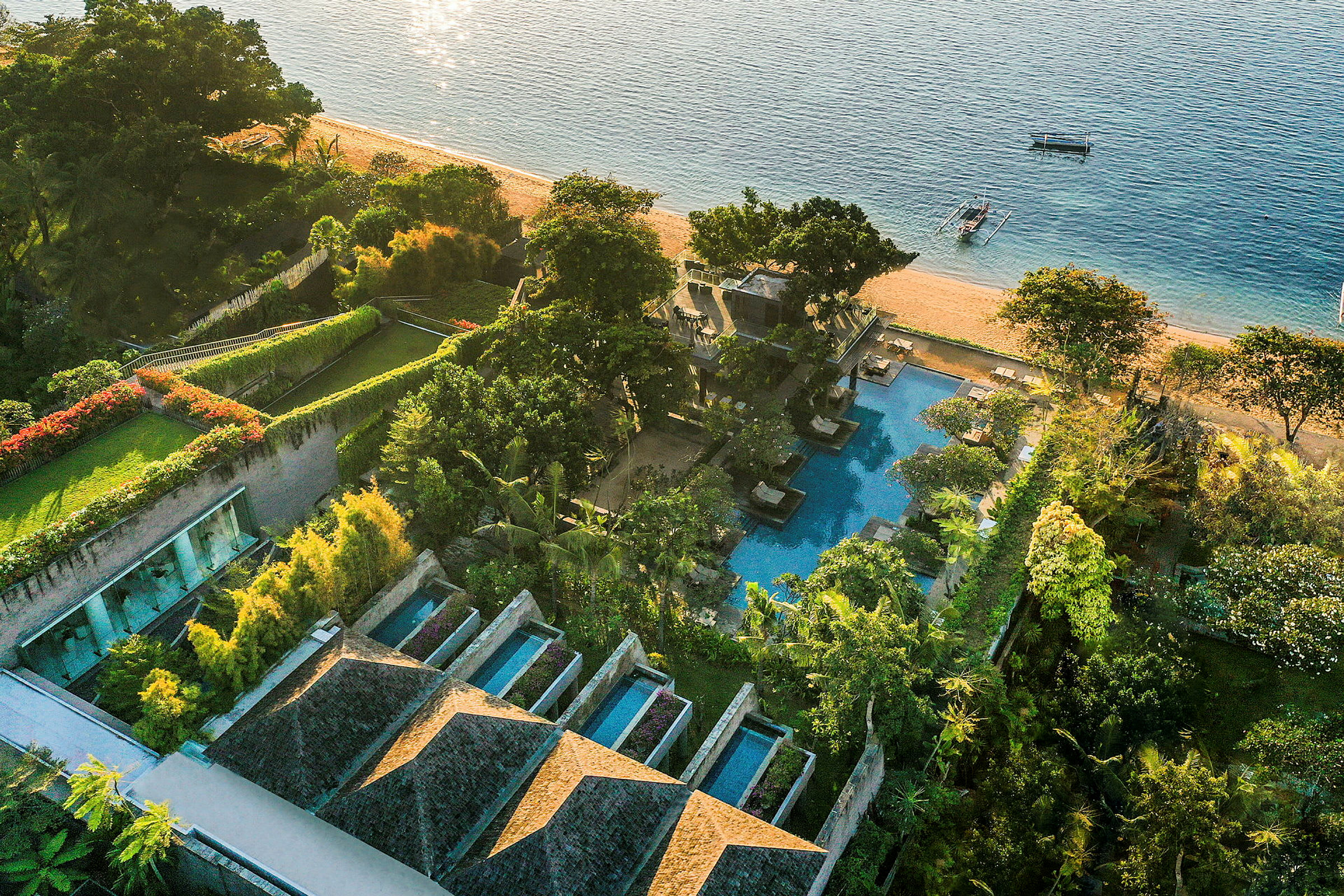 Et fugleperspektiv af et strandnært luksushotel med swimmingpools, grønne haver og stranden som grænser til havet. (AI-genereret tekst)