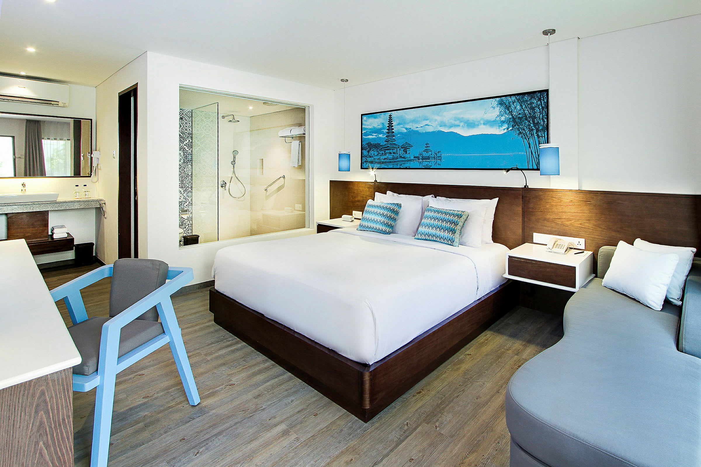Et moderne hotelværelse med en stor seng, et skrivebord med en stol, en sofa og et badeværelse med glasvæg. (AI-genereret tekst)