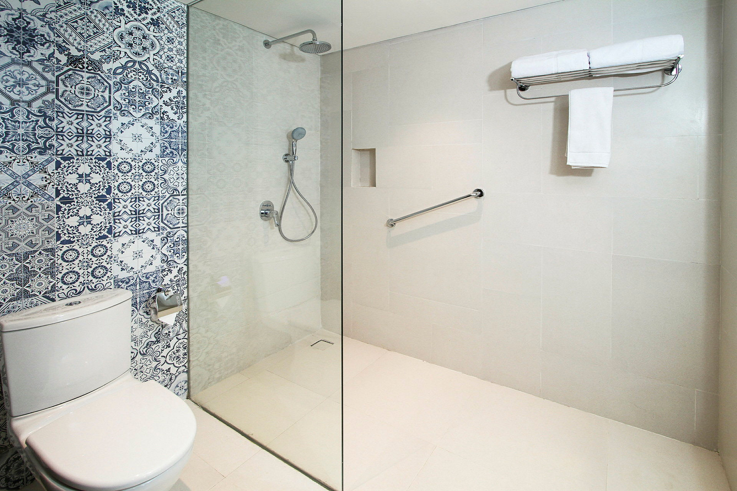 Badeværelse med moderne design, bruseområde med glasvæg og flisevæg med blå og hvide mønstre. Toilettet er ved siden af. (AI-genereret tekst)