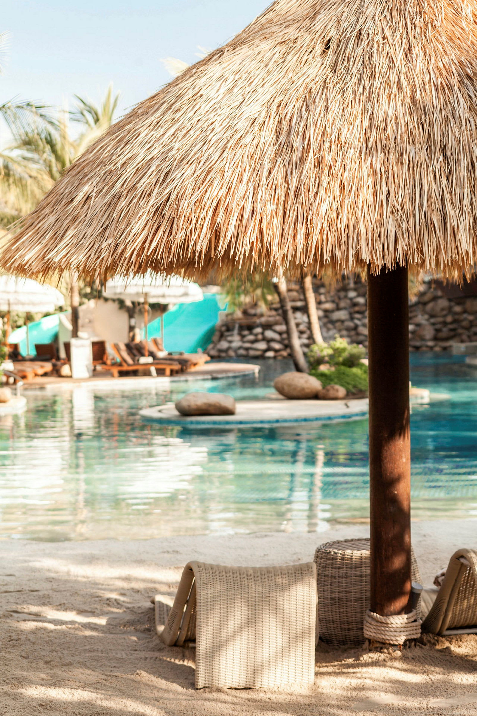 Et stråtag på en parasol ved en pool med liggestole og grønne planter i baggrunden. (AI-genereret tekst)