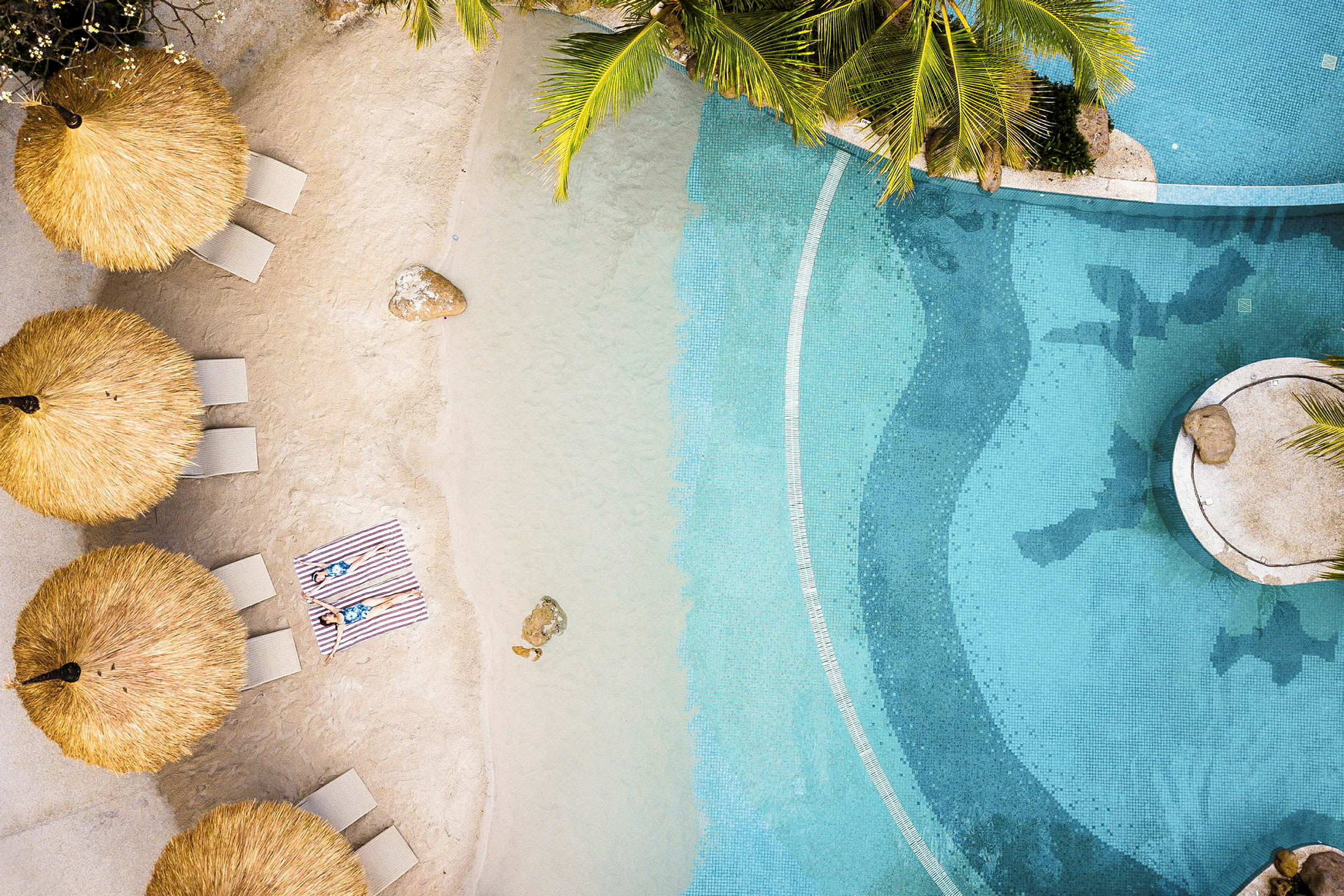 En strand med liggestole placeret under stråtag ved en pool. (AI-genereret tekst)