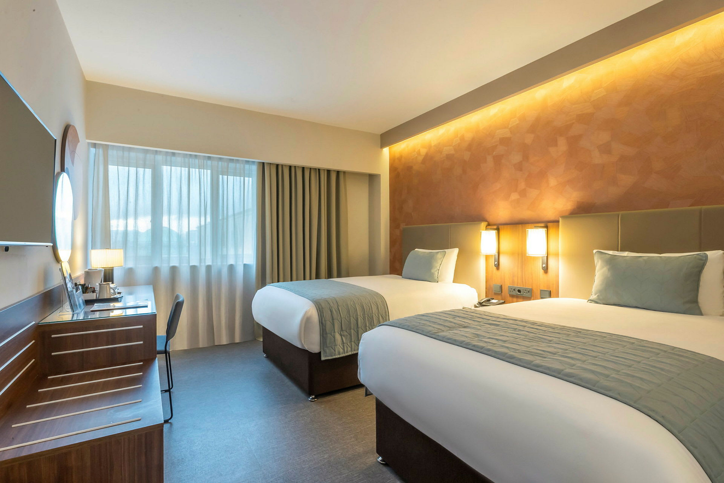 Et hotelværelse med to enkeltsenge, skrivebord og vindue. (AI-genereret tekst)