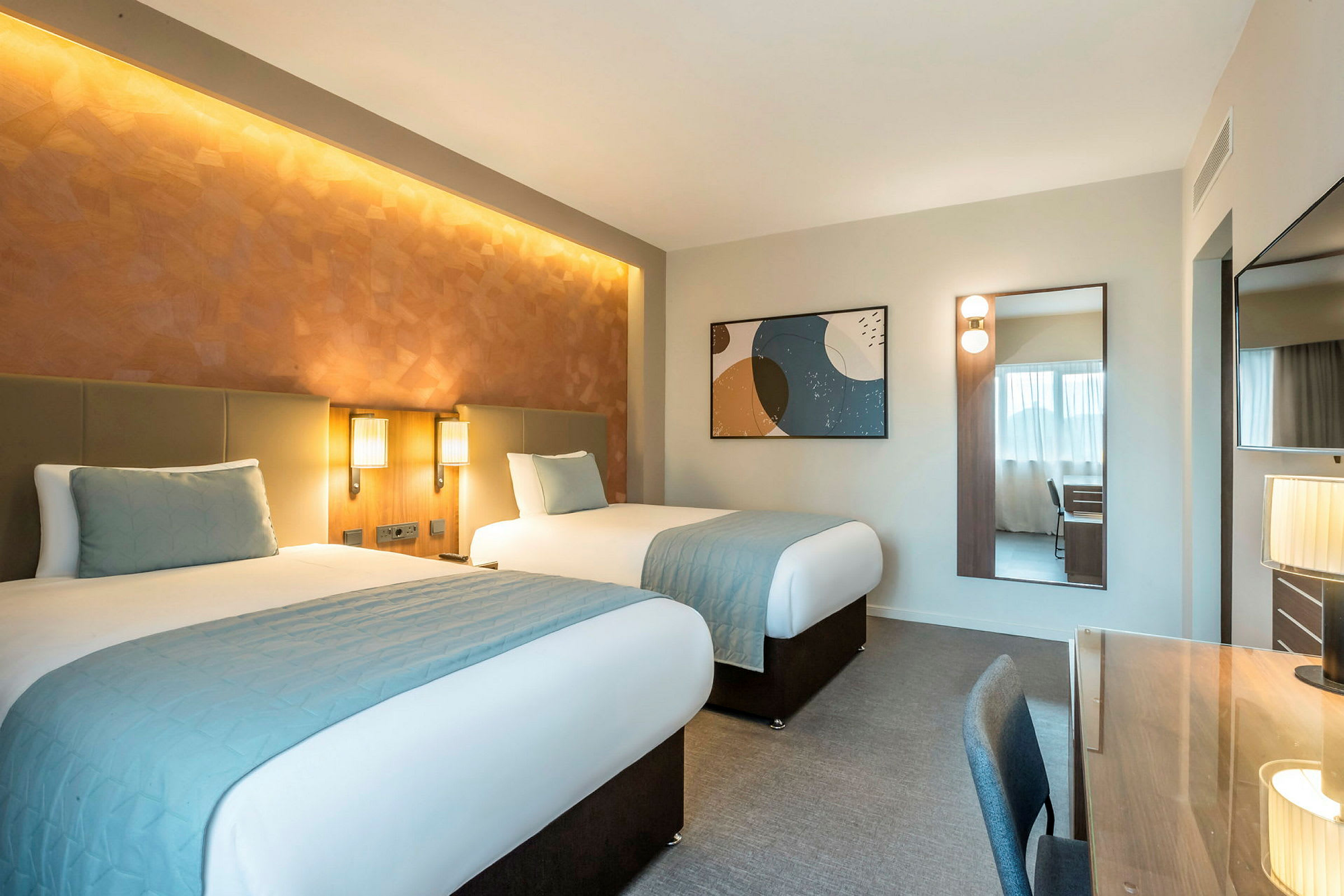 Hotelværelse med to enkeltsenge, skrivebord og spejl. (AI-genereret tekst)
