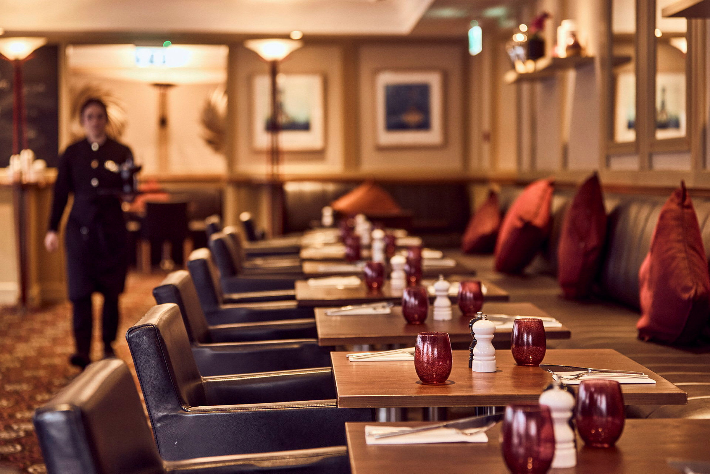En restaurant med dækkede borde, røde glas og mørke stole kan ses på billedet. (AI-genereret tekst)