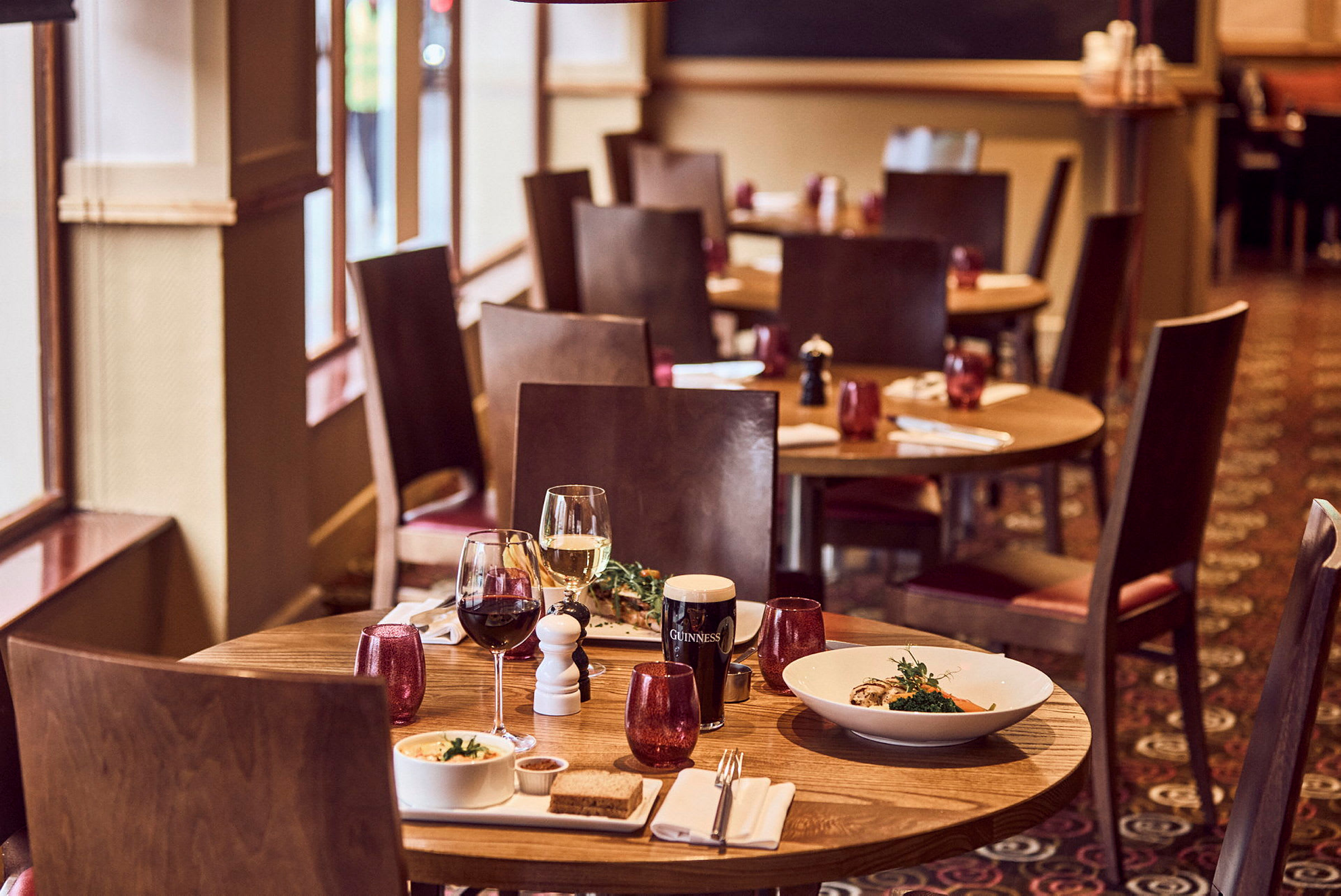 Et restaurantbord med to vinglas og serveret mad på tallerkener. (AI-genereret tekst)