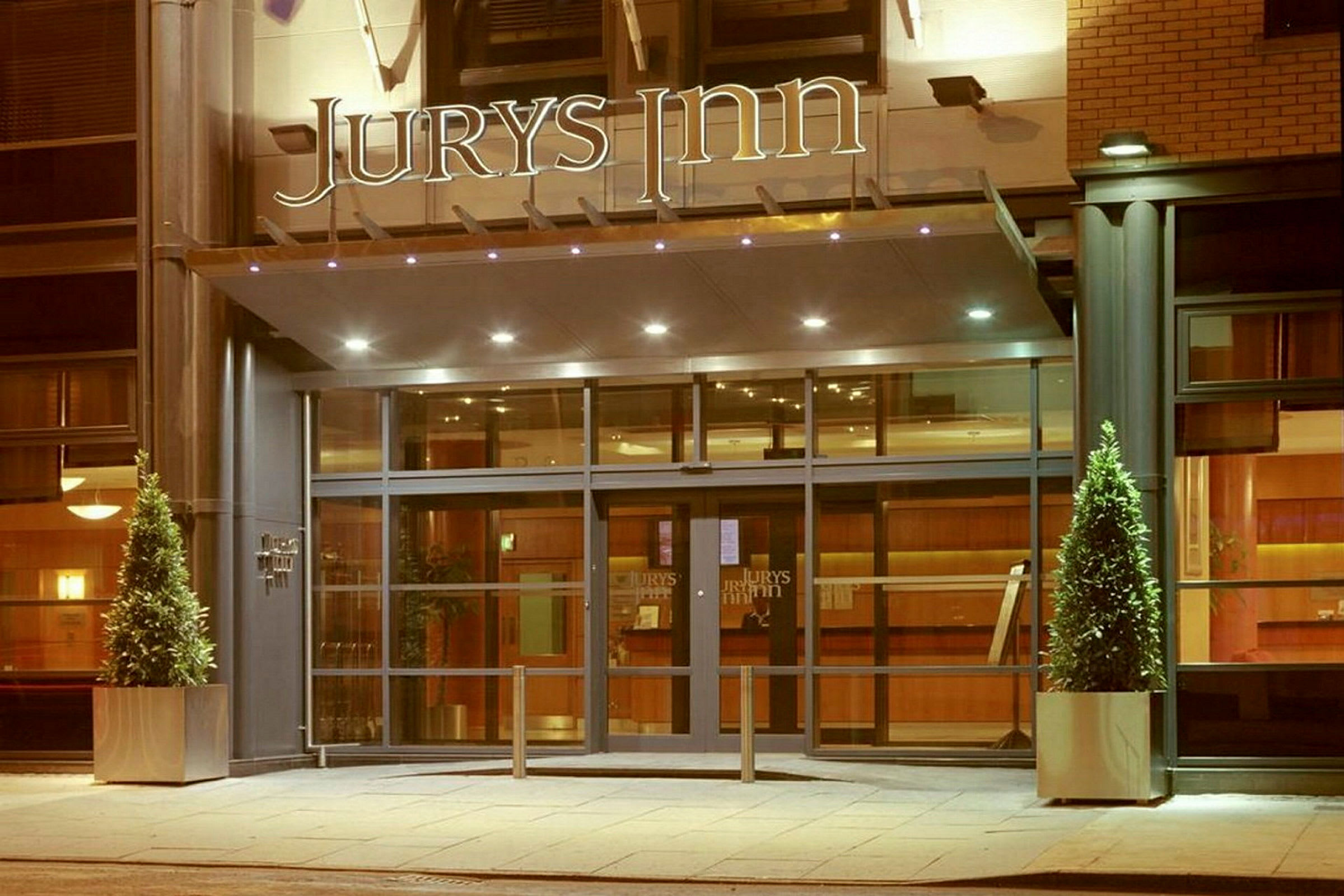 Hotelindgang med glasdøre og skiltet 'Jurys Inn' ovenfor. (AI-genereret tekst)