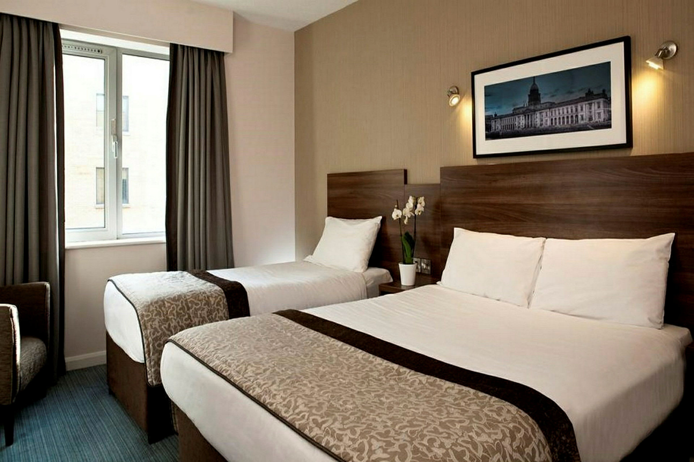 Hotelværelse med to senge, en plante på natbordet, et vindue og en vægdekoration. (AI-genereret tekst)