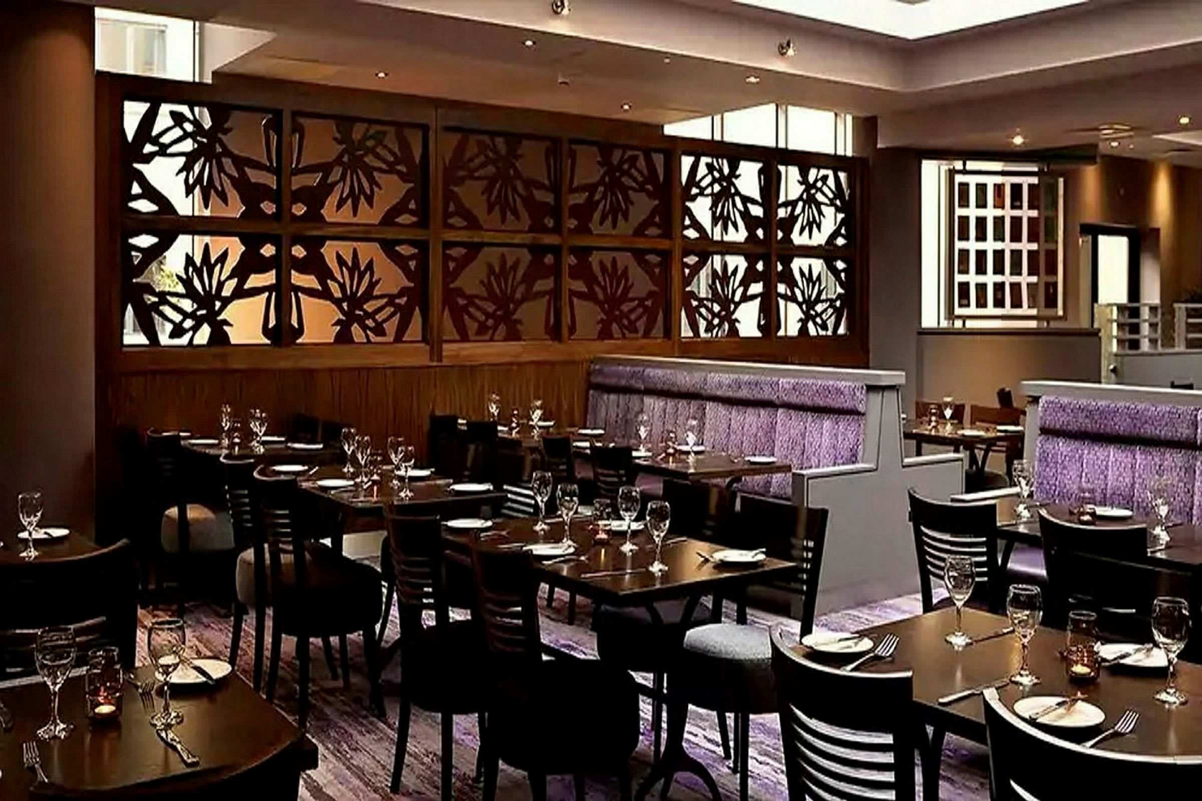 En stilfuld restaurant med borde og stole opstillet, en dekorativ væg med blomsterdesign og lilla detaljer på siddepladser. (AI-genereret tekst)