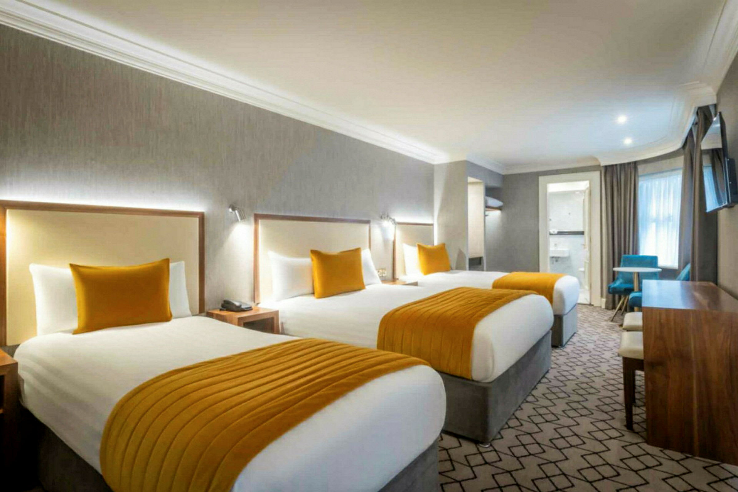 Hotelværelse med tre senge, orange detaljer og skrivebord. (AI-genereret tekst)