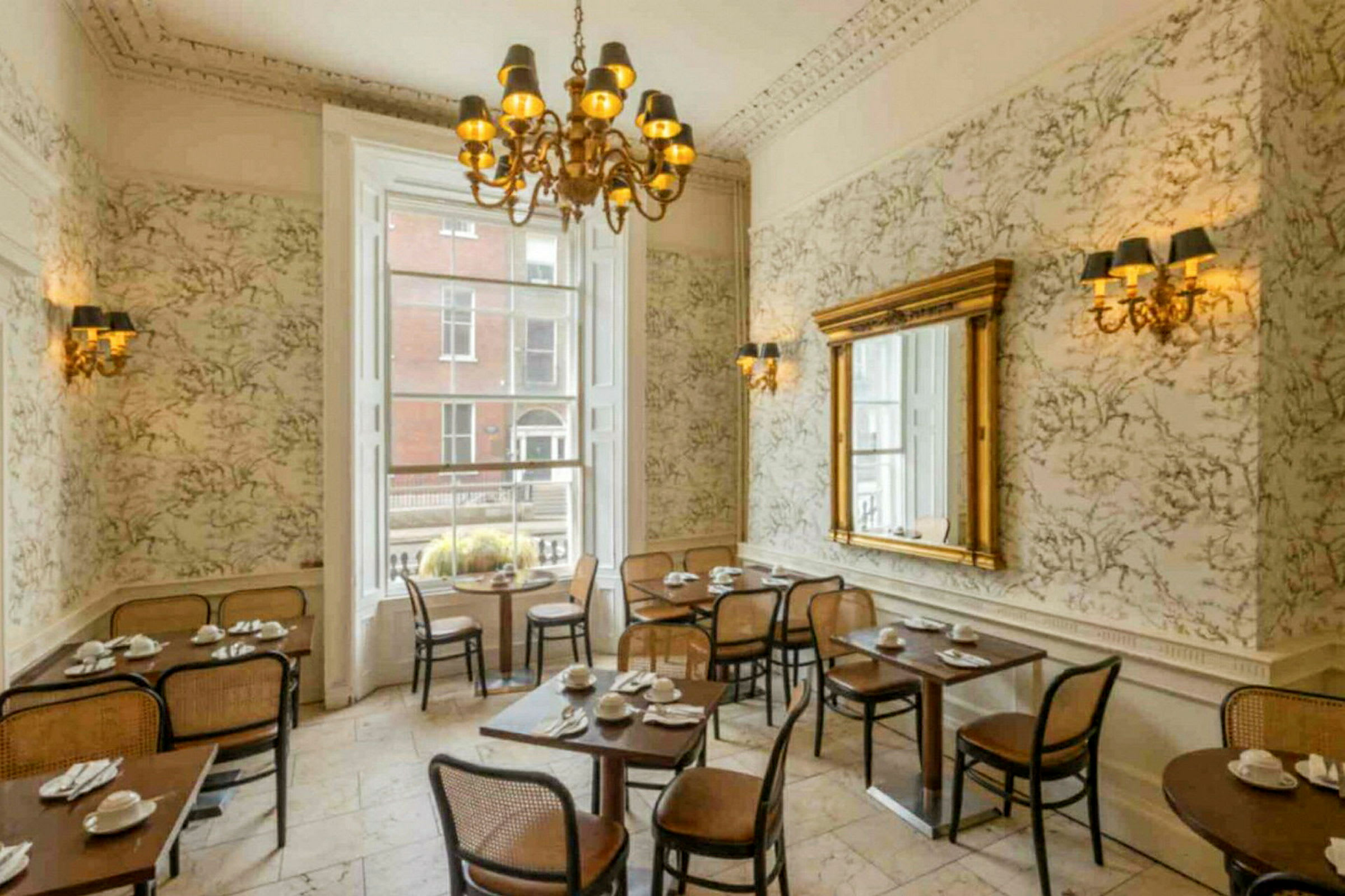 En restaurantinteriør med klassisk indretning, borde og stole, stor spejl og en lysekrone. (AI-genereret tekst)