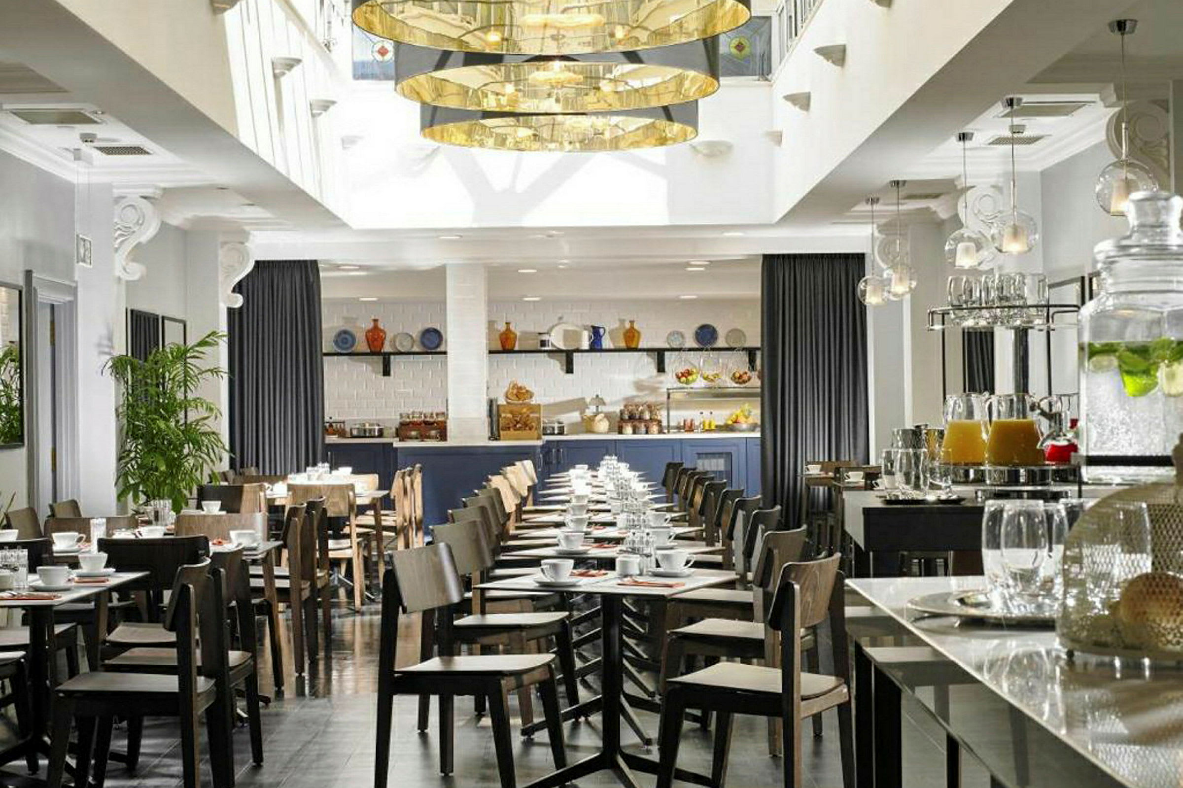 En moderne indrettet café eller restaurant med borde og stole, en serveringsdisk og dekorationer som planter og hængende lamper. (AI-genereret tekst)