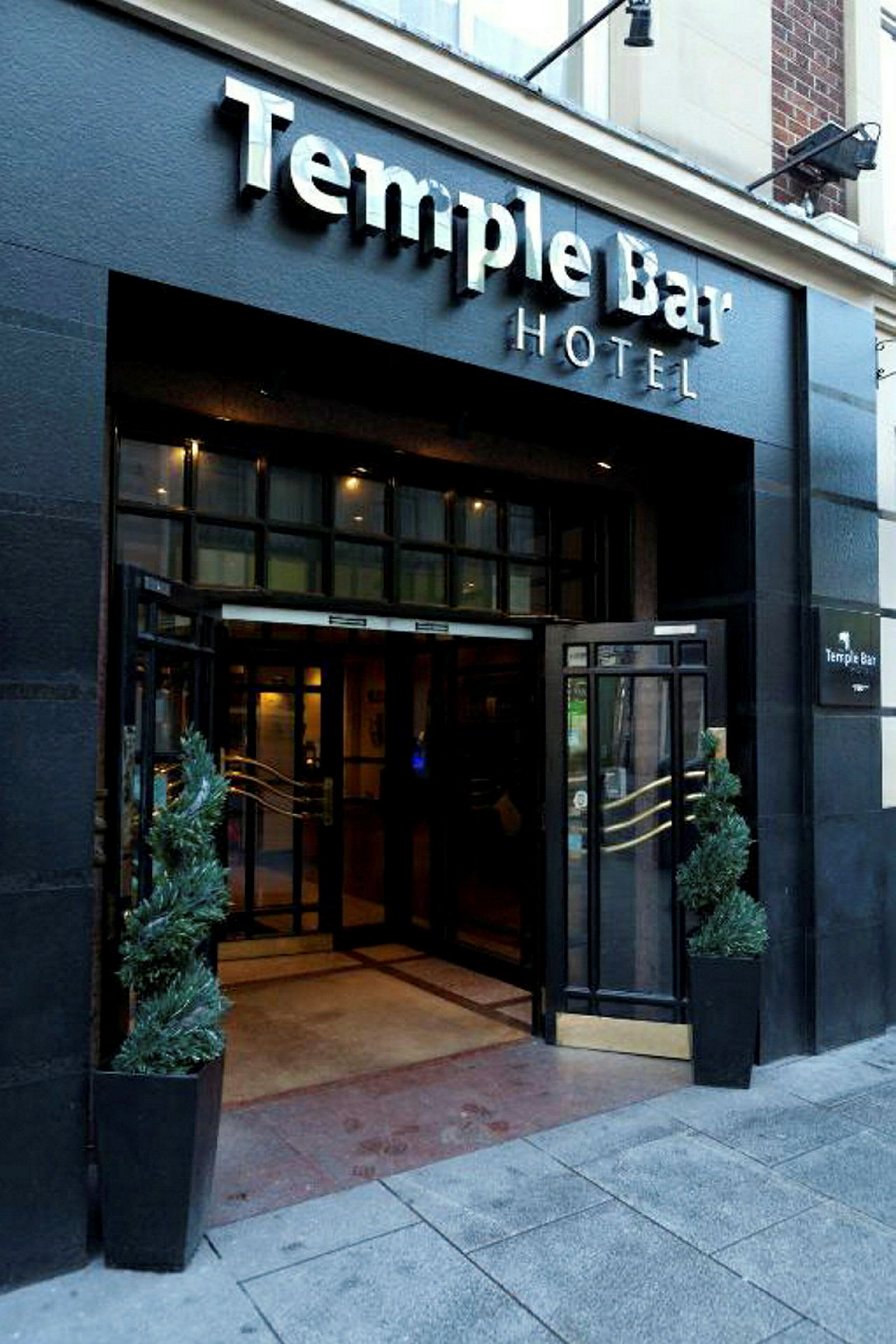 Indgangen til Temple Bar Hotel med skilt ovenfor og to potteplanter på hver side af døren. (AI-genereret tekst)