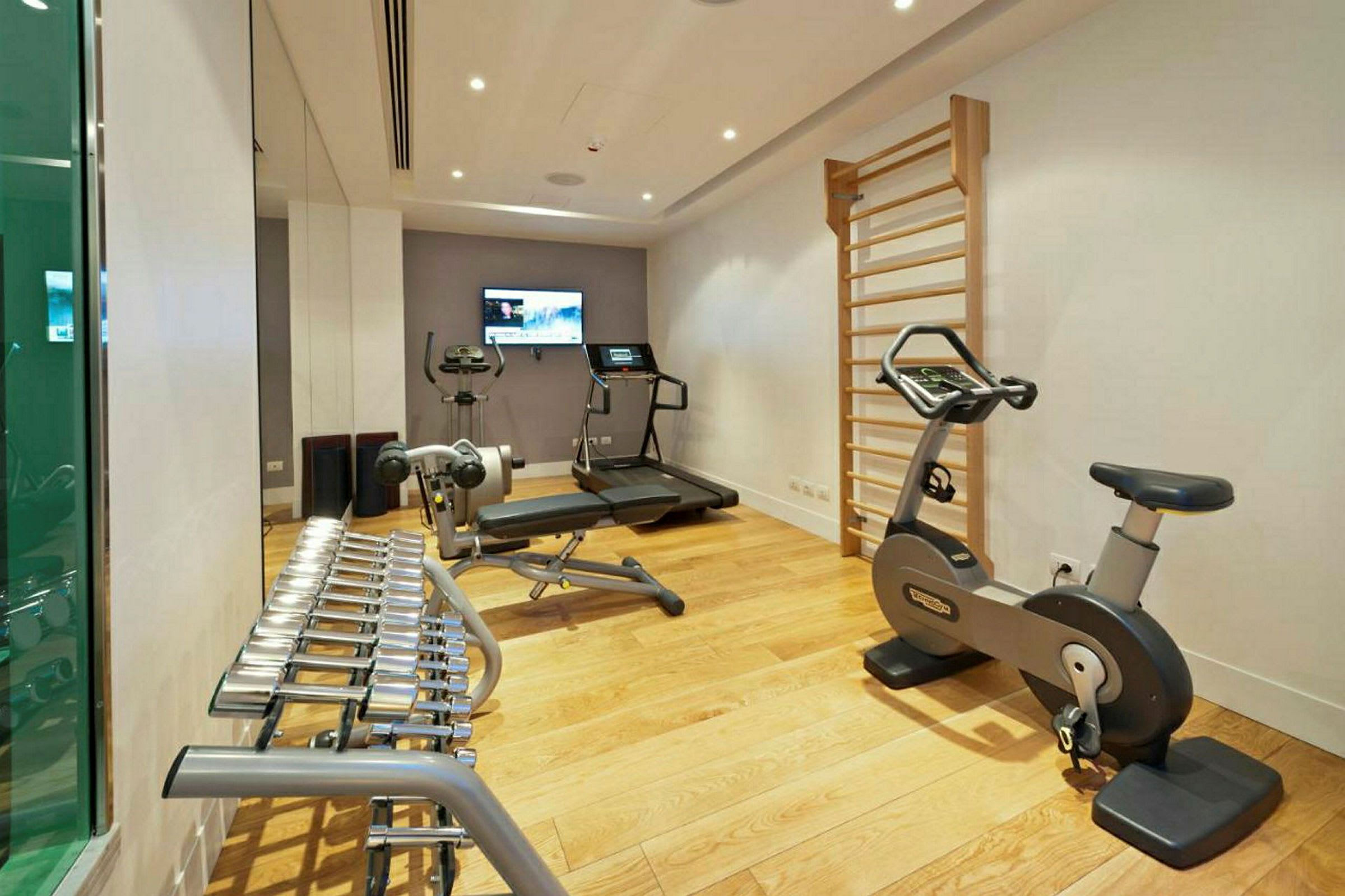 Et fitnessrum med træningsudstyr inklusive løbebånd, motionscykel, vægtløftningsmaskine og ribbevæg. (AI-genereret tekst)