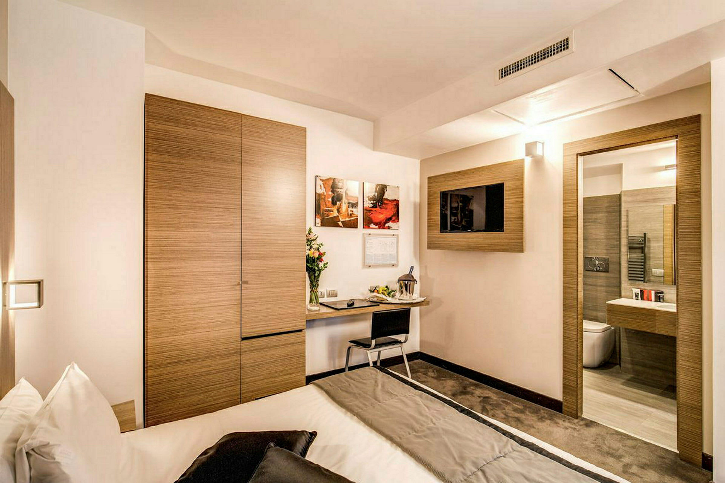 Et moderne hotelværelse med et skrivebord, en seng og et fjernsyn på væggen. (AI-genereret tekst)