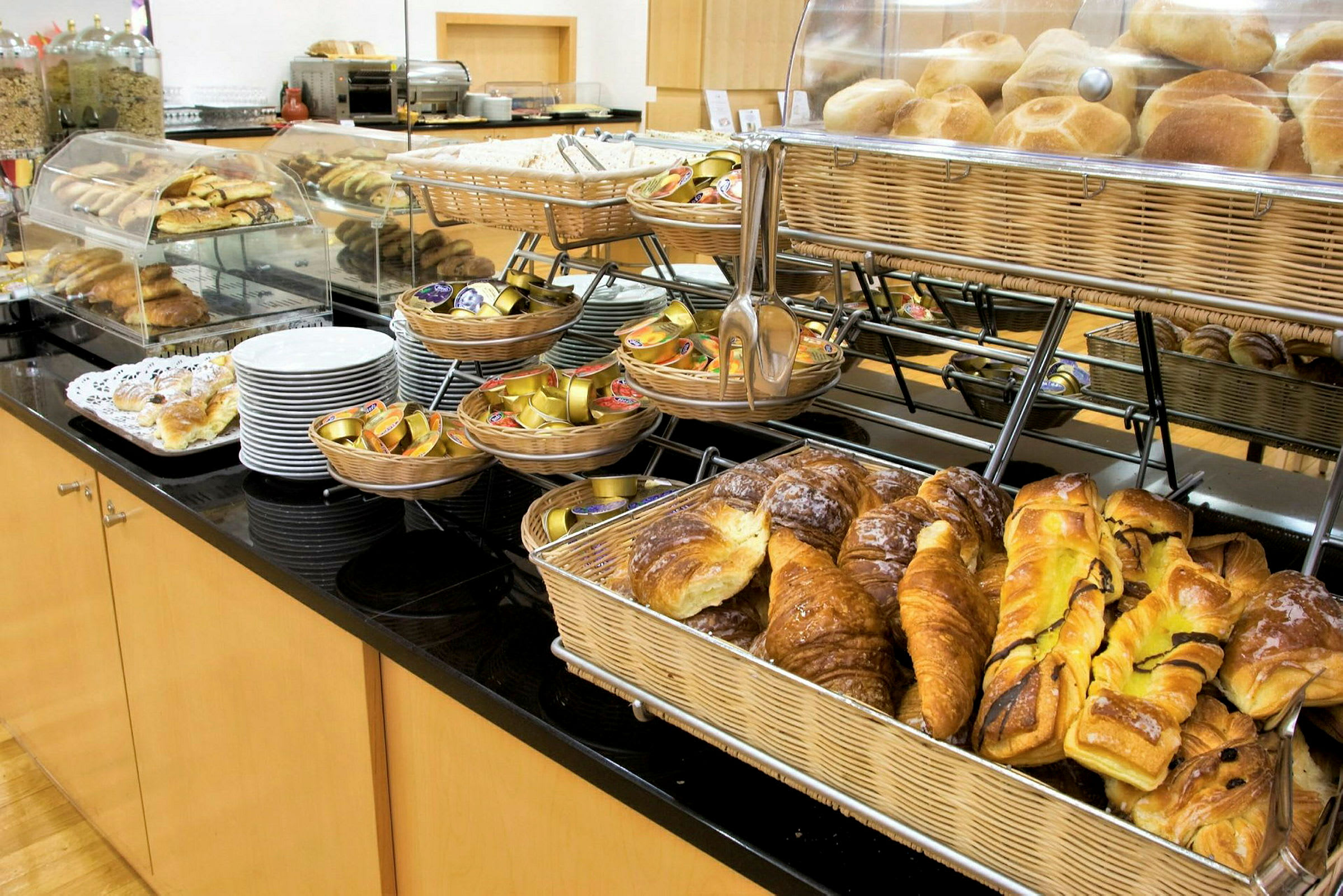 Et morgenmadsbuffetbord med forskellige typer bagværk, brød i kurve og portioner af syltetøj. (AI-genereret tekst)