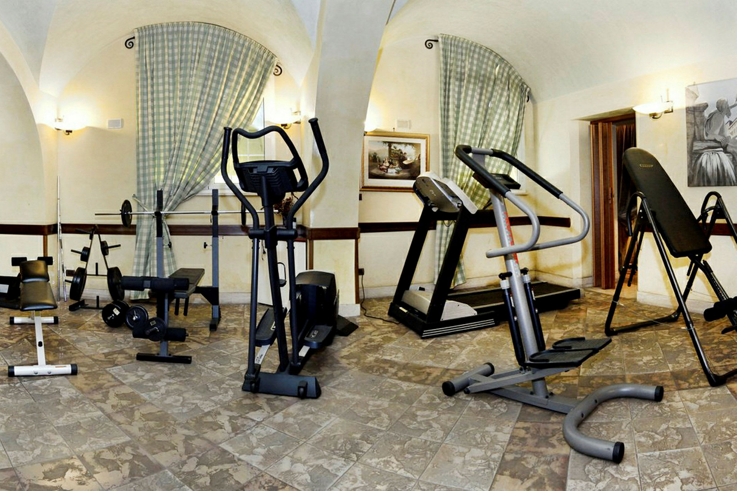 Et rum indrettet som fitnesscenter med træningsudstyr som motionscykler, løbebånd og styrkemaskiner. (AI-genereret tekst)