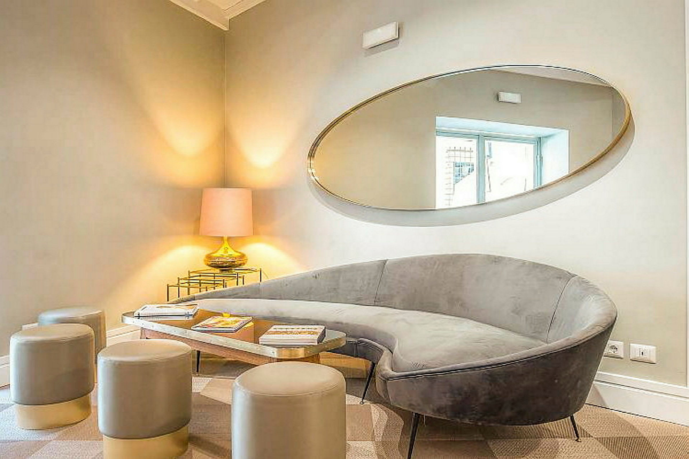 En elegant dagligstue med en grå sofa, moderne skamler, et spejlet bord og en bordlampe placeret i hjørnet. (AI-genereret tekst)
