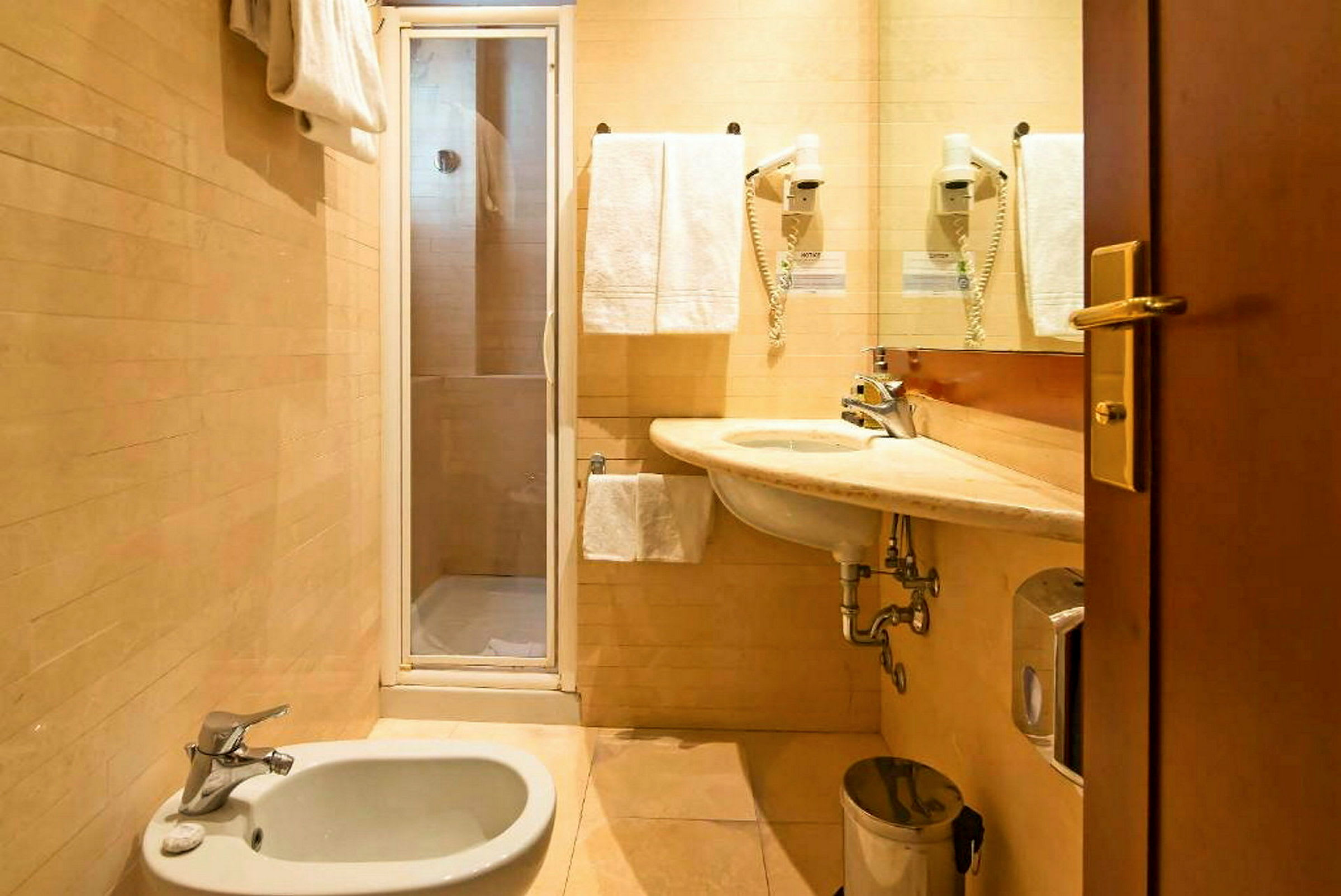 Et badeværelse med bruser, håndvask, bidet og håndklæder. (AI-genereret tekst)