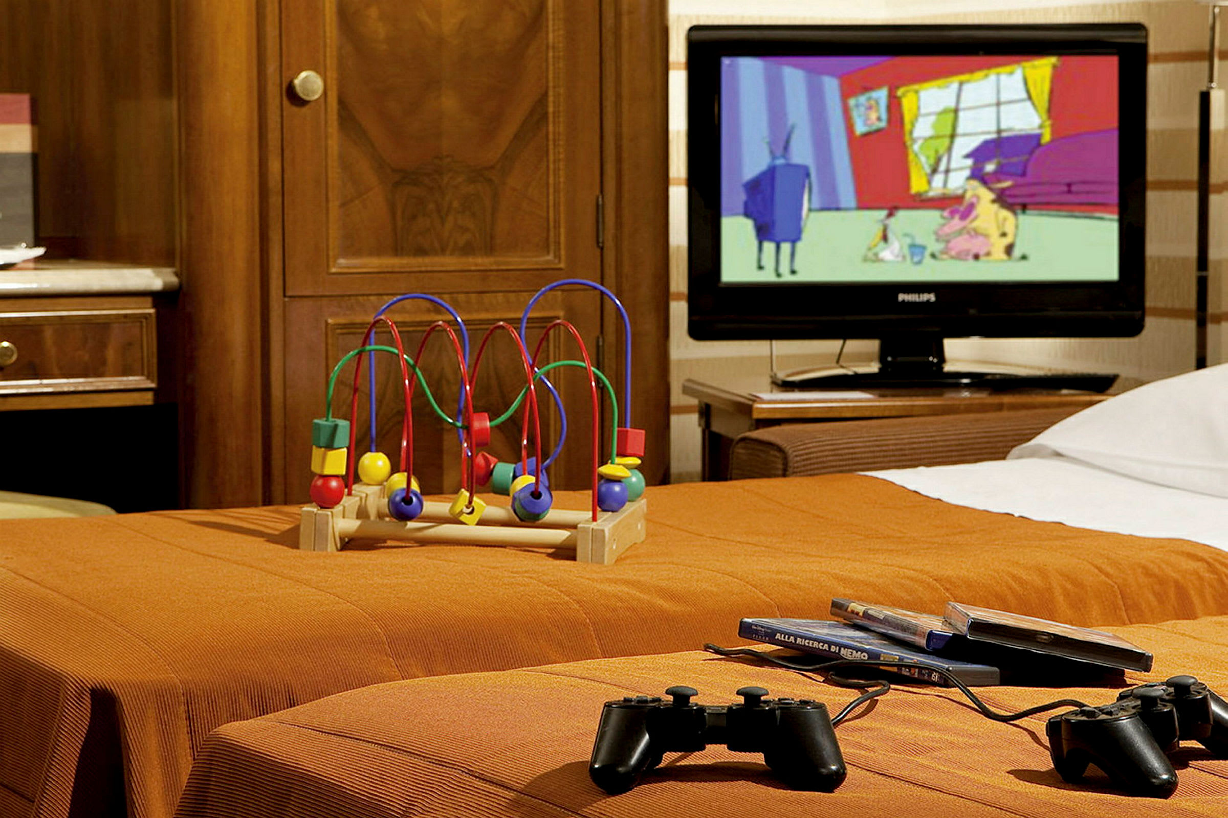Et hotelværelse med legetøj, tv og spil-controllere på en orange seng. (AI-genereret tekst)