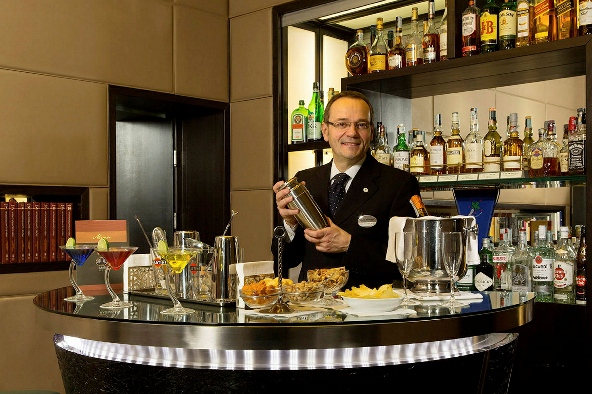 En bartender holder en shaker ved en bardisk fyldt med flasker og cocktails. (AI-genereret tekst)