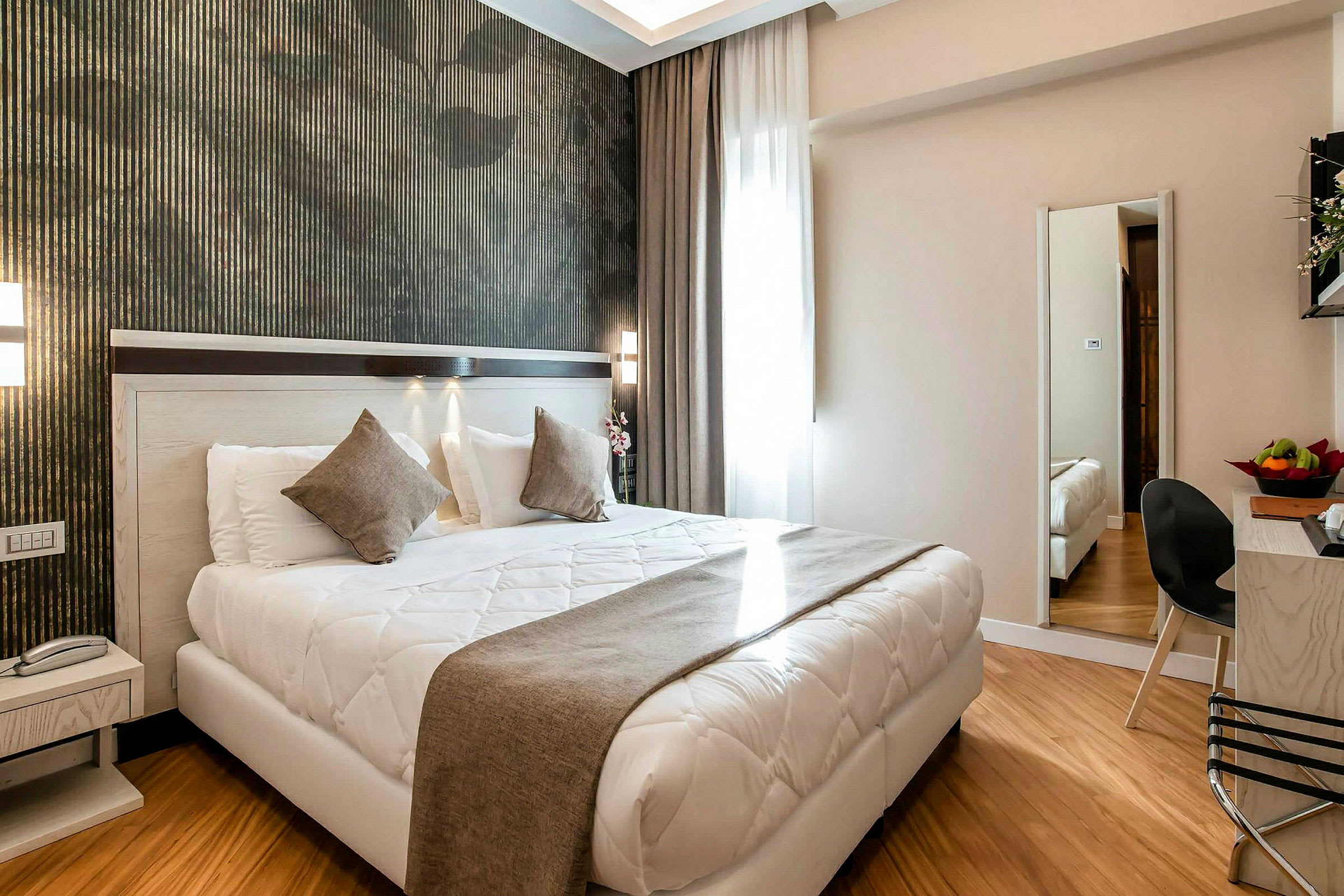 Moderne indrettet hotelværelse med dobbeltseng, natbord, spejl og siddeområde. (AI-genereret tekst)