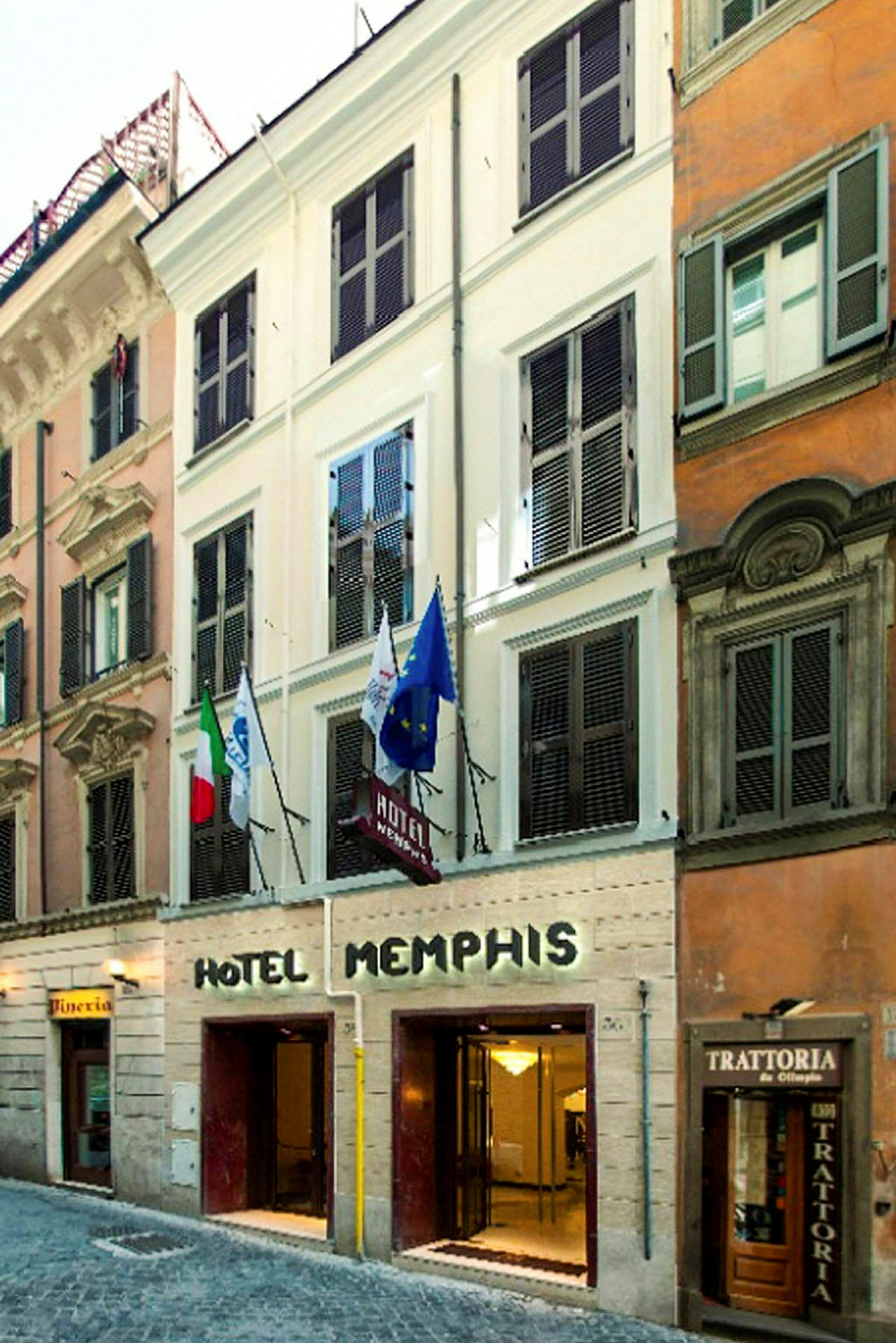 Facaden af Hotel Memphis med indgang i gadeplan og flag synlige over. (AI-genereret tekst)