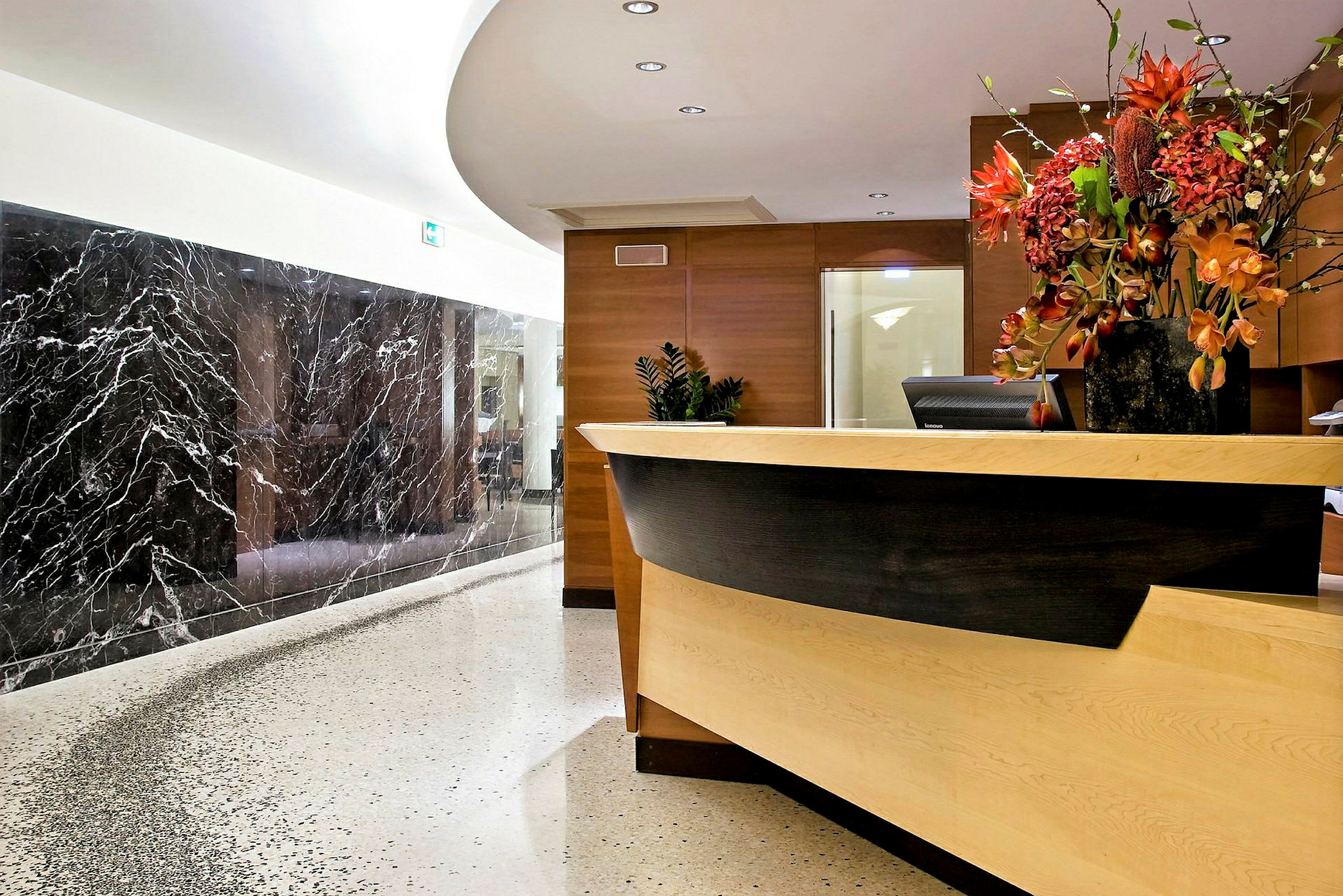 En receptionsdisk på et hotel, dekoreret med en stor vase med blomster og omgivet af marmordetaljer og elegant belysning. (AI-genereret tekst)