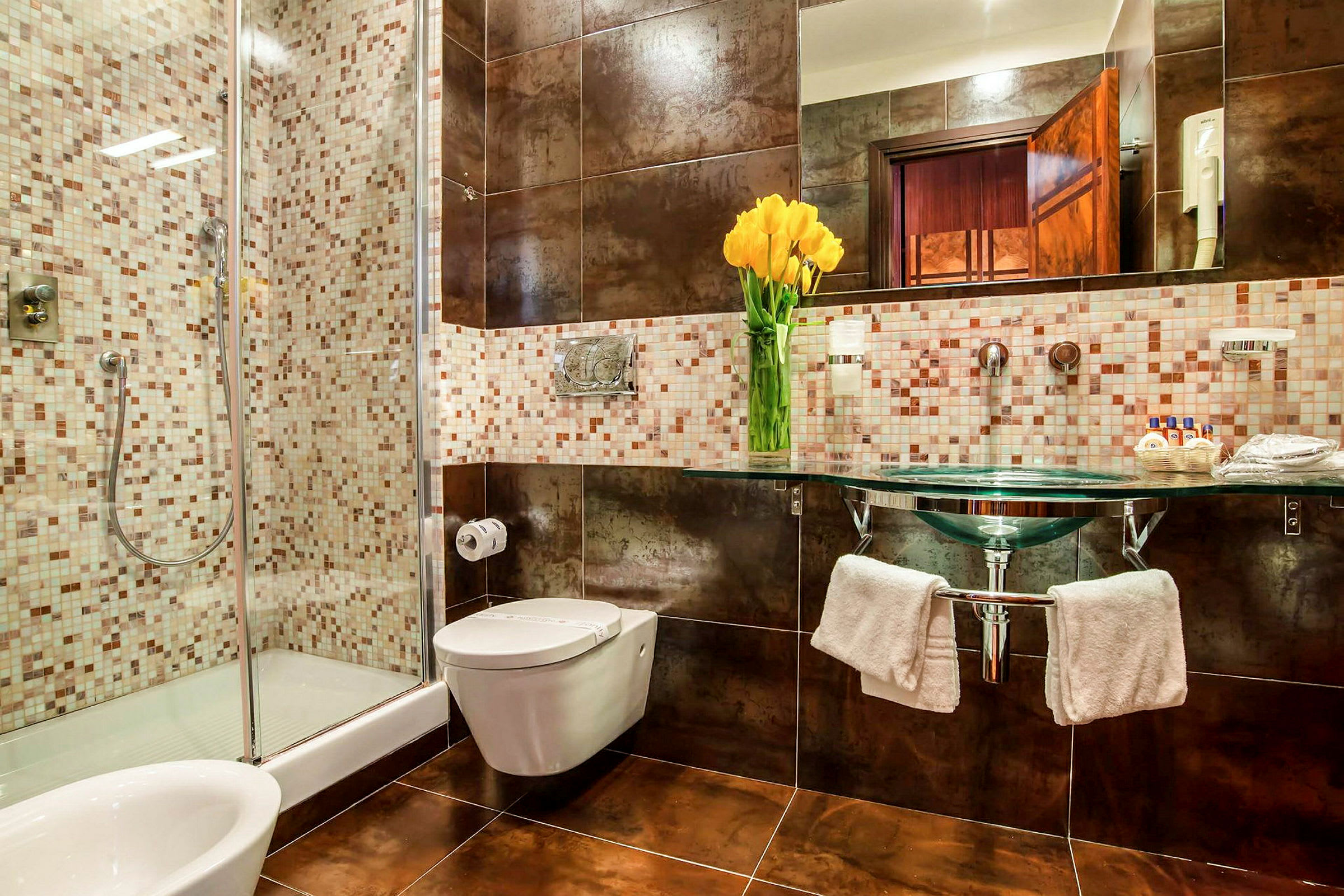 Et moderne badeværelse med brusekabine, toilet, håndvask med spejl og en vase med gule blomster. (AI-genereret tekst)