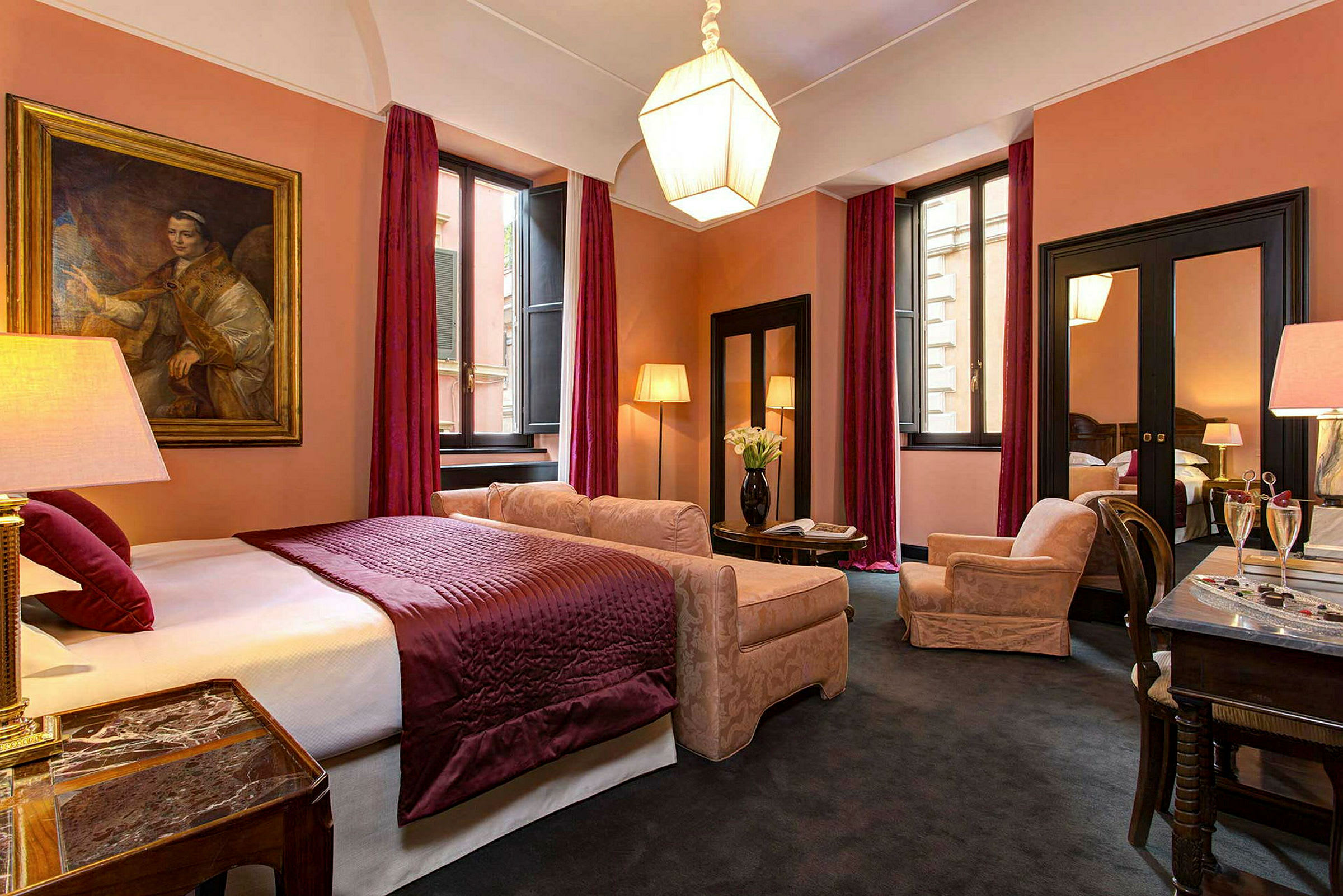 Et elegant hotelværelse med en dobbeltseng, lilla sengetæppe og matchende gardiner, sammen med komfortable lænestole og et bord. (AI-genereret tekst)