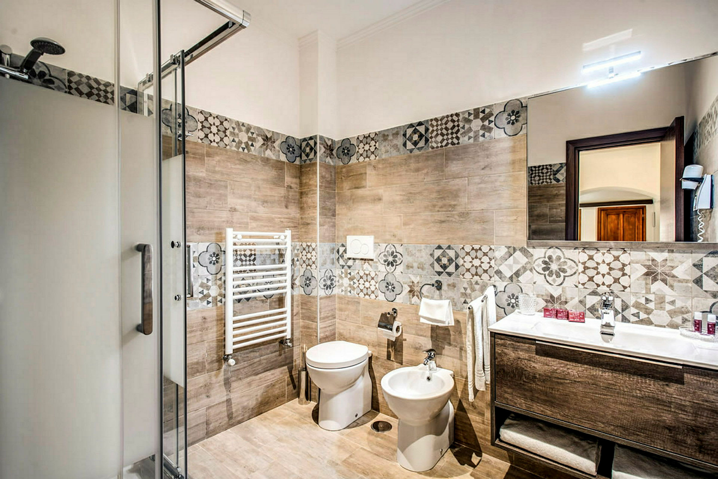 Et badeværelse med brusekabine, toilet, bidet, håndvask og dekorative vægfliser. (AI-genereret tekst)