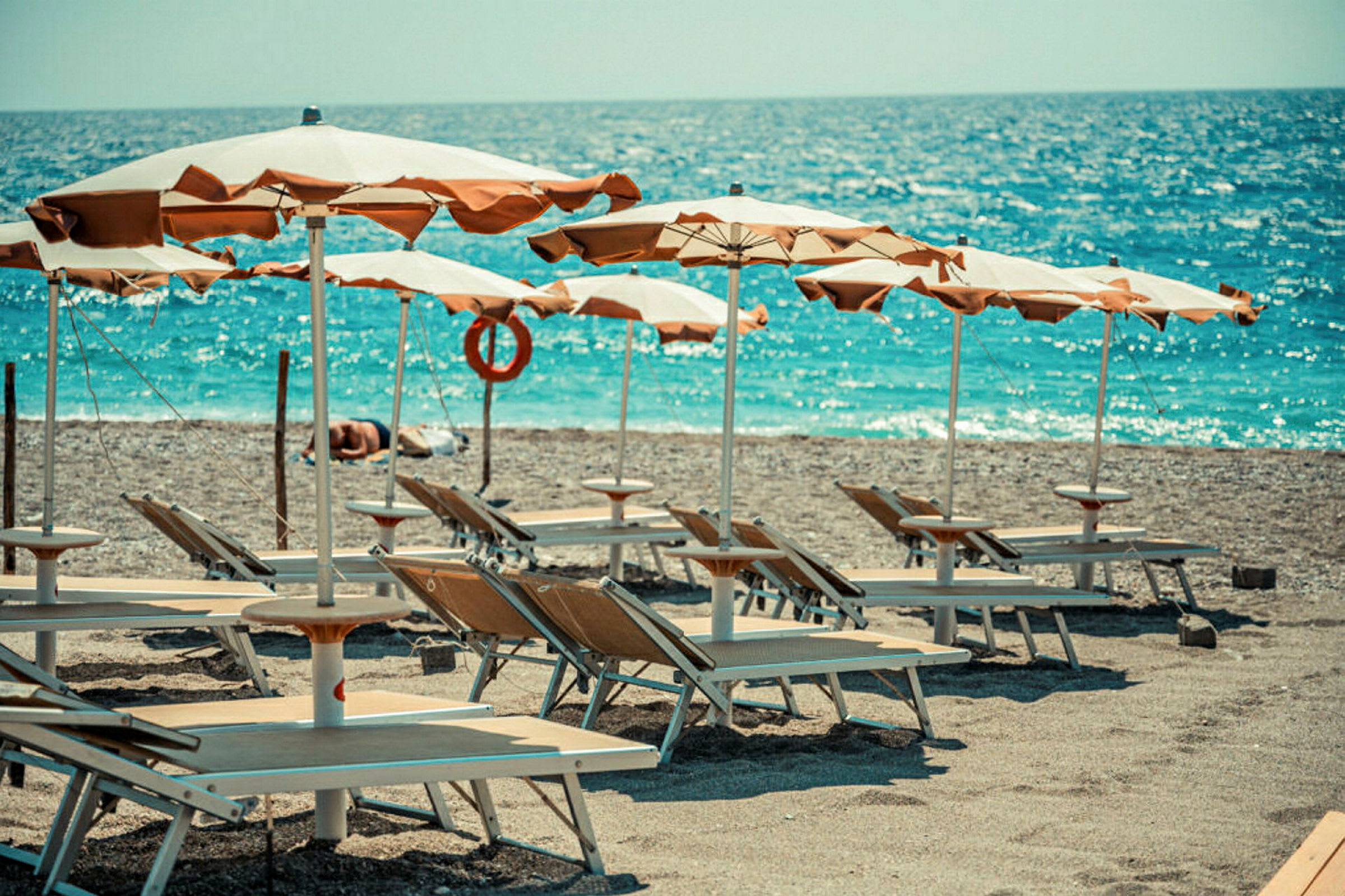 Liggestole og parasoller på en strand ved havet. (AI-genereret tekst)