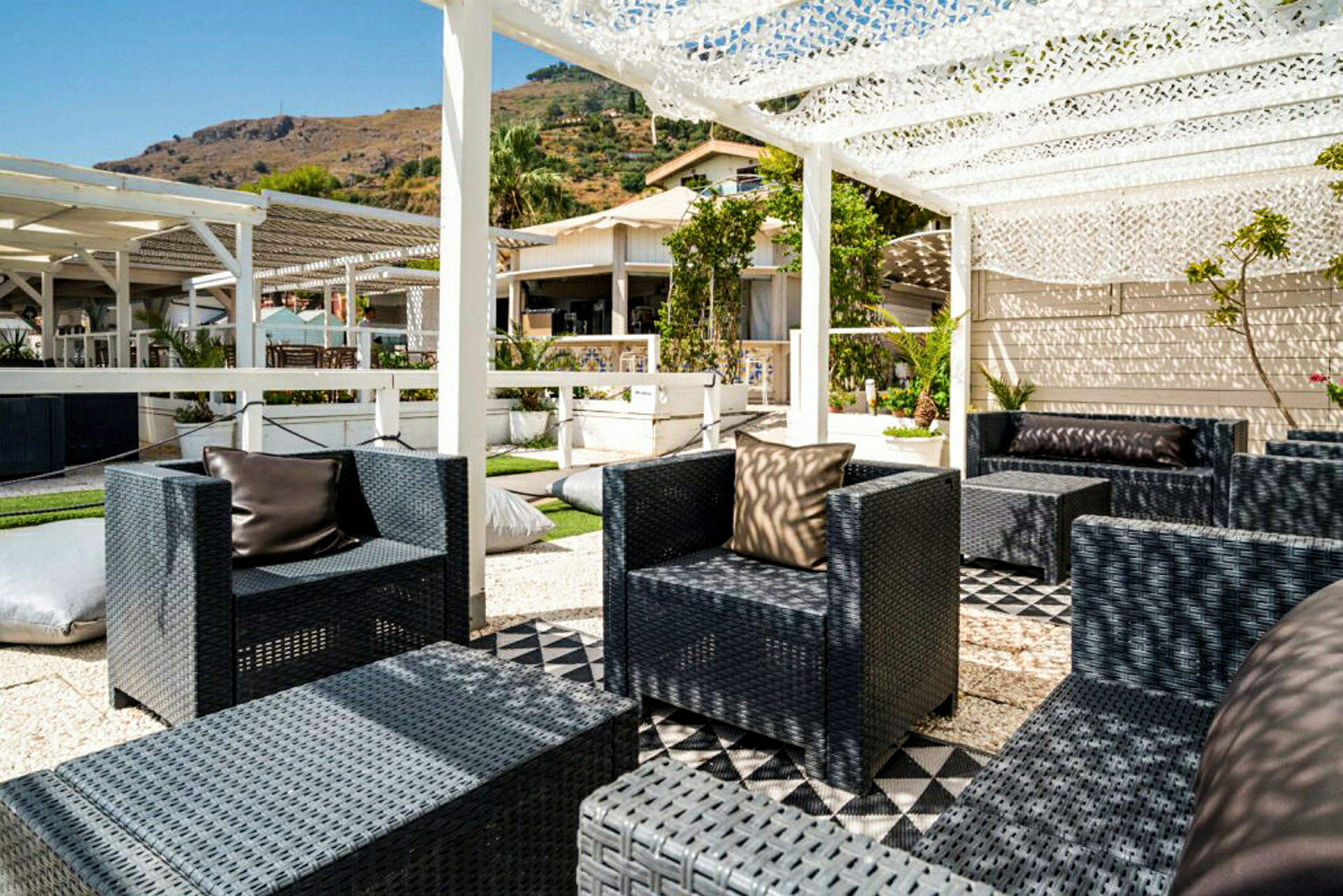 En udendørs lounge med flettede stole og borde under en pergola. (AI-genereret tekst)