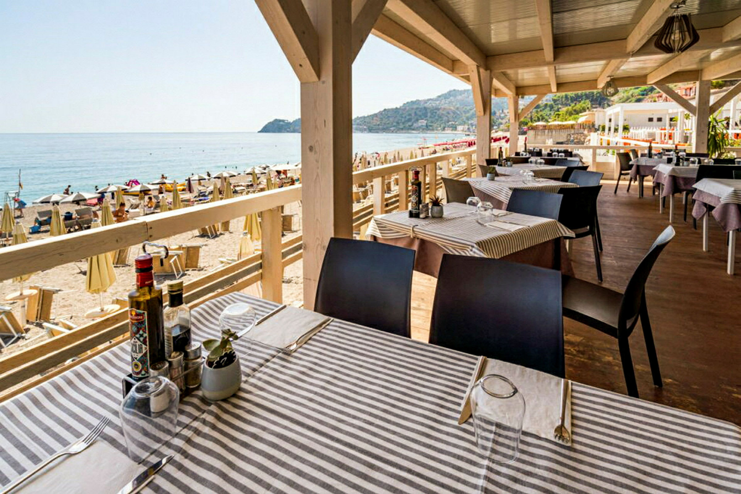 En strandrestaurant med udsigt over havet og stranden, med dækkede borde og liggestole i baggrunden. (AI-genereret tekst)