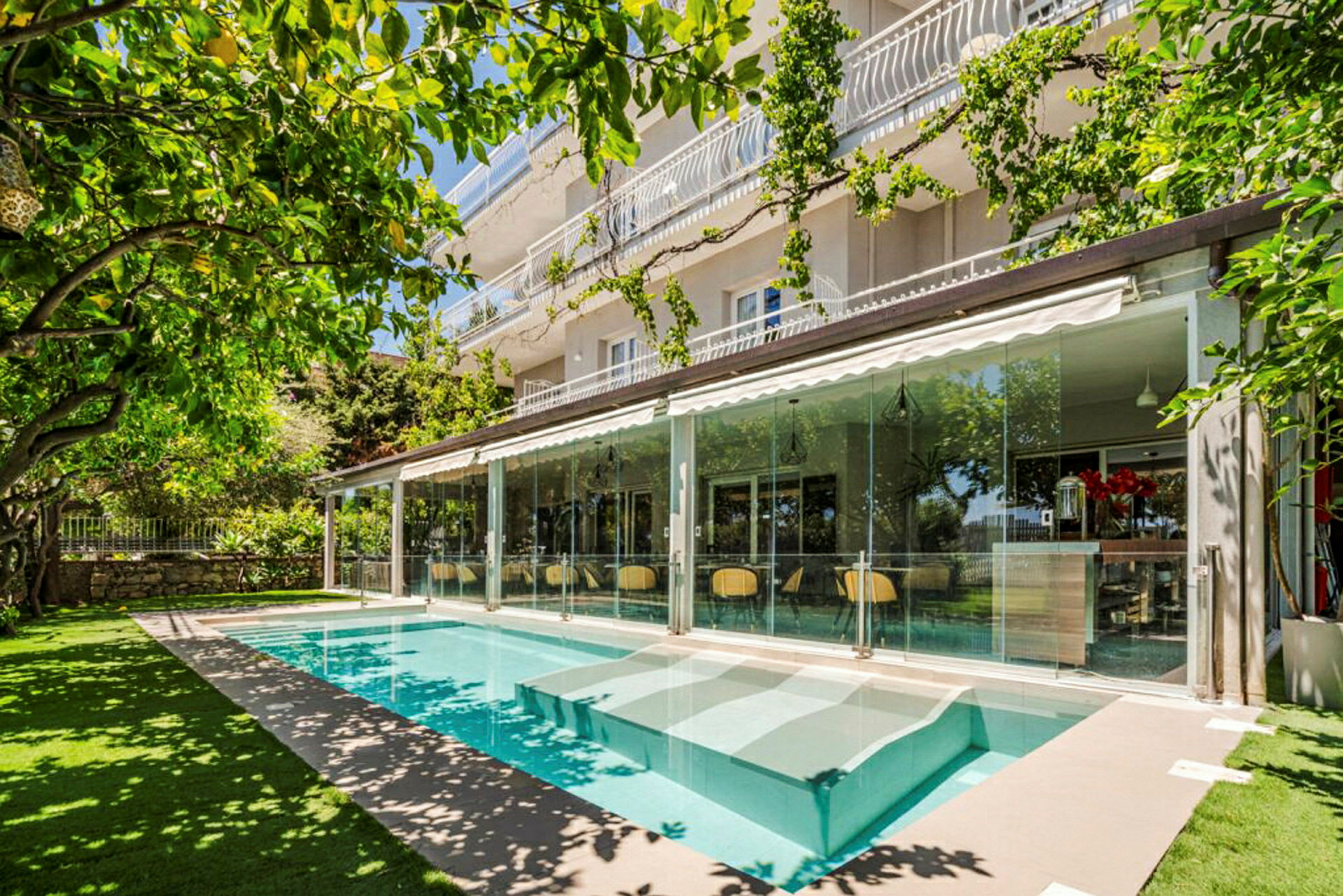 En moderne bygning med glasfacade ved siden af en pool og omgivet af frodigt grønt. (AI-genereret tekst)