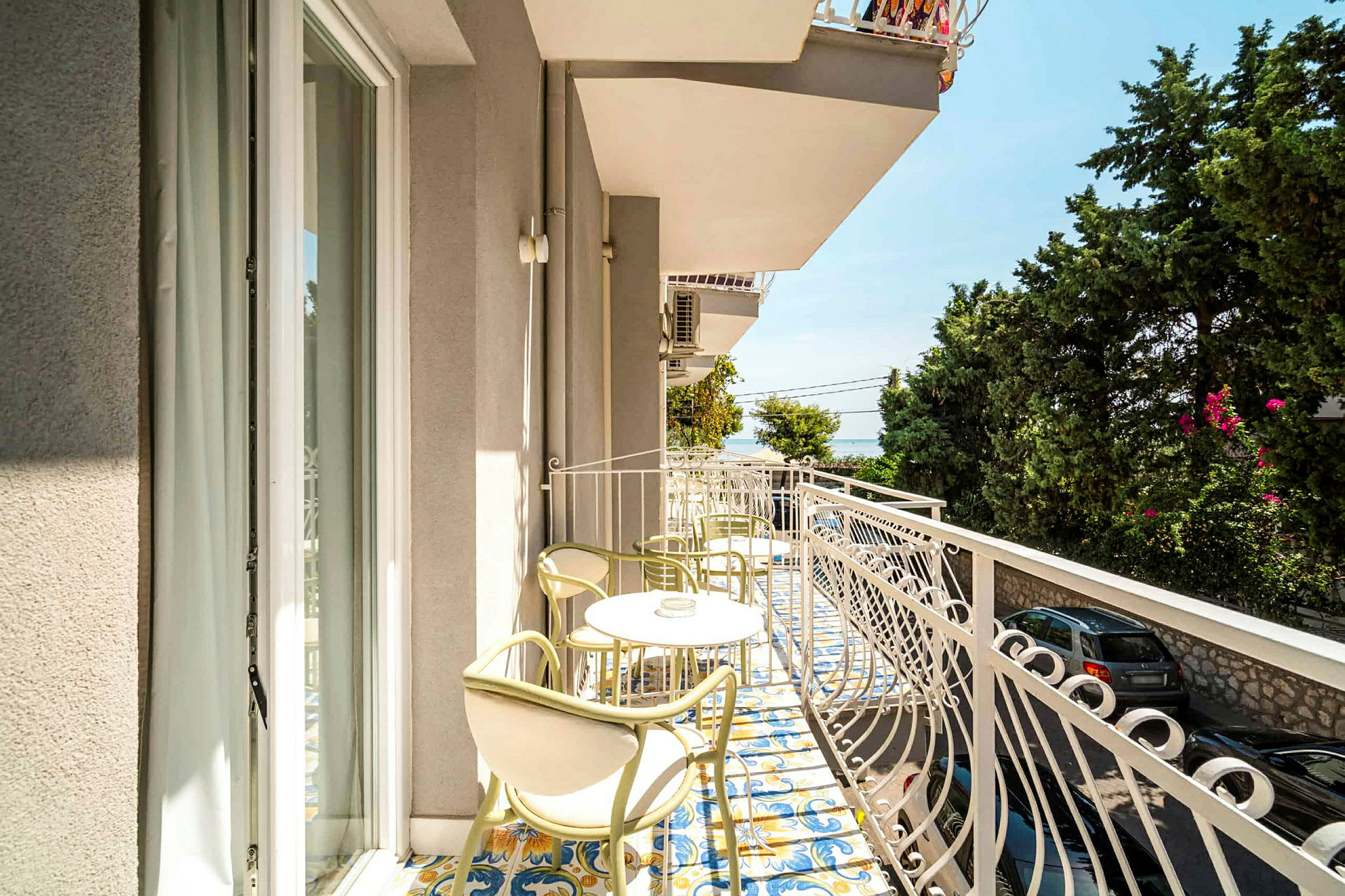 En balkon med borde og stole samt udsigt over vegetation og havet. (AI-genereret tekst)